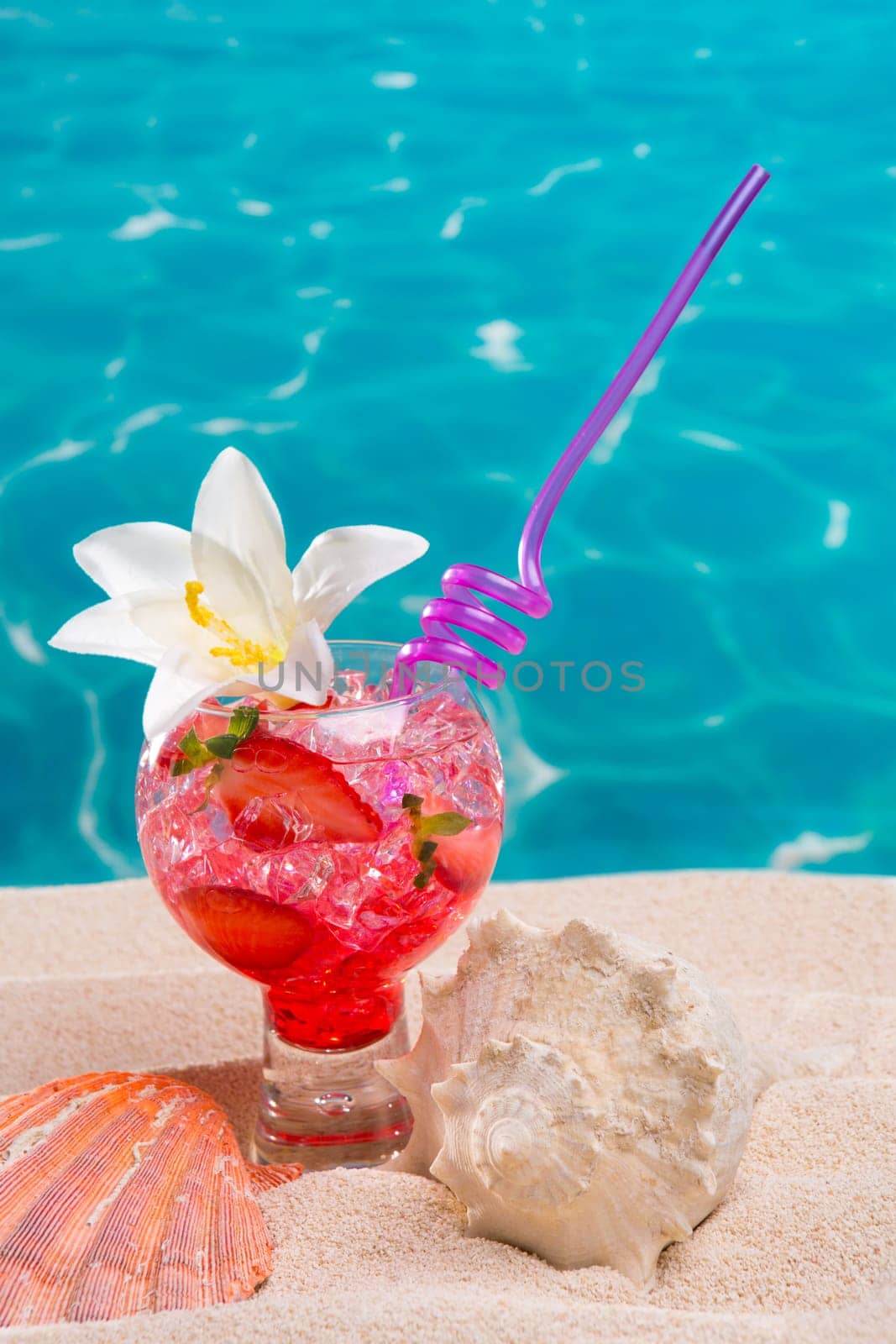 Strawberry cocktail on beach sand with seashell and turquoise beach