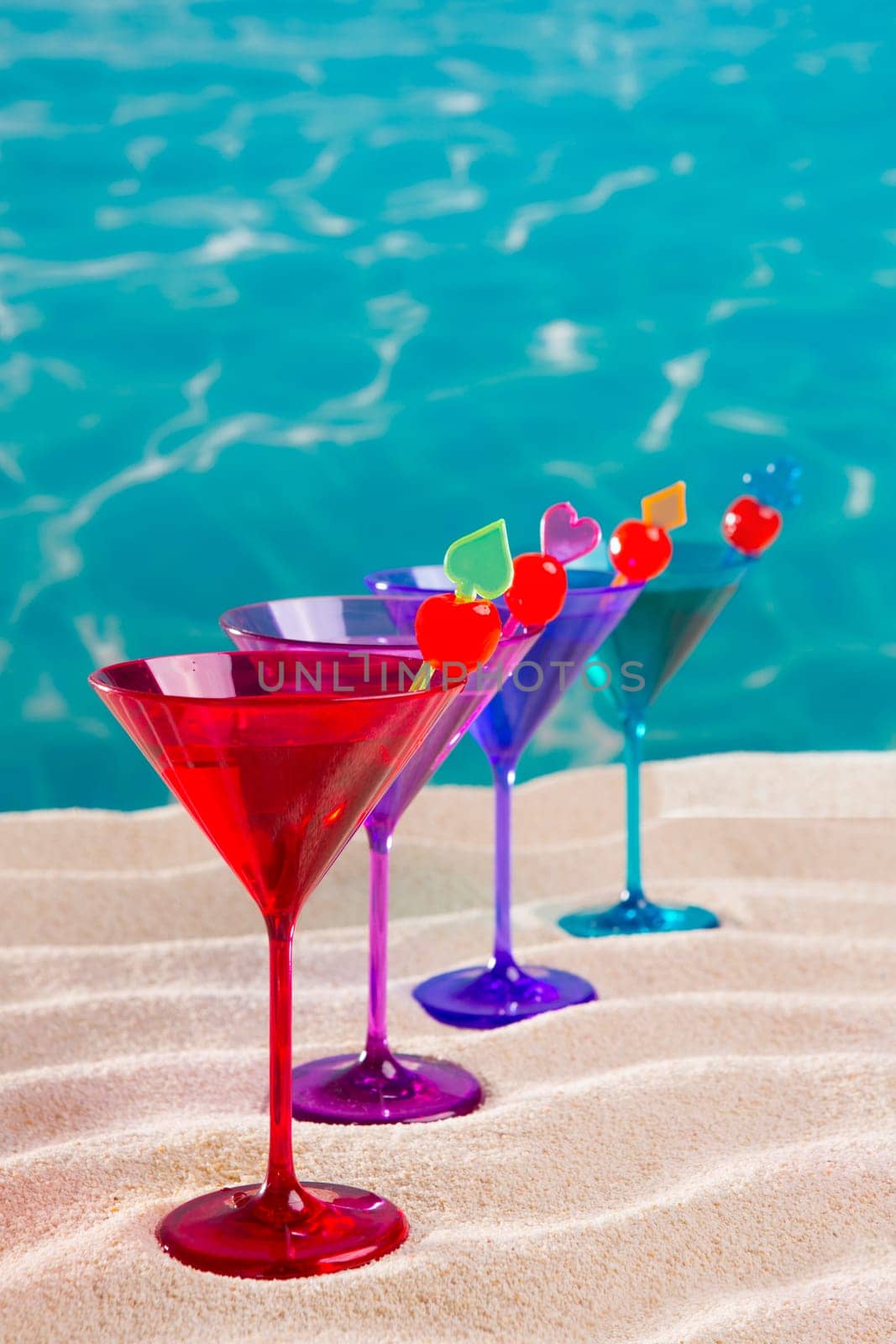 colorful cocktail in a row with cherry on tropical sand beach of turquoise sea