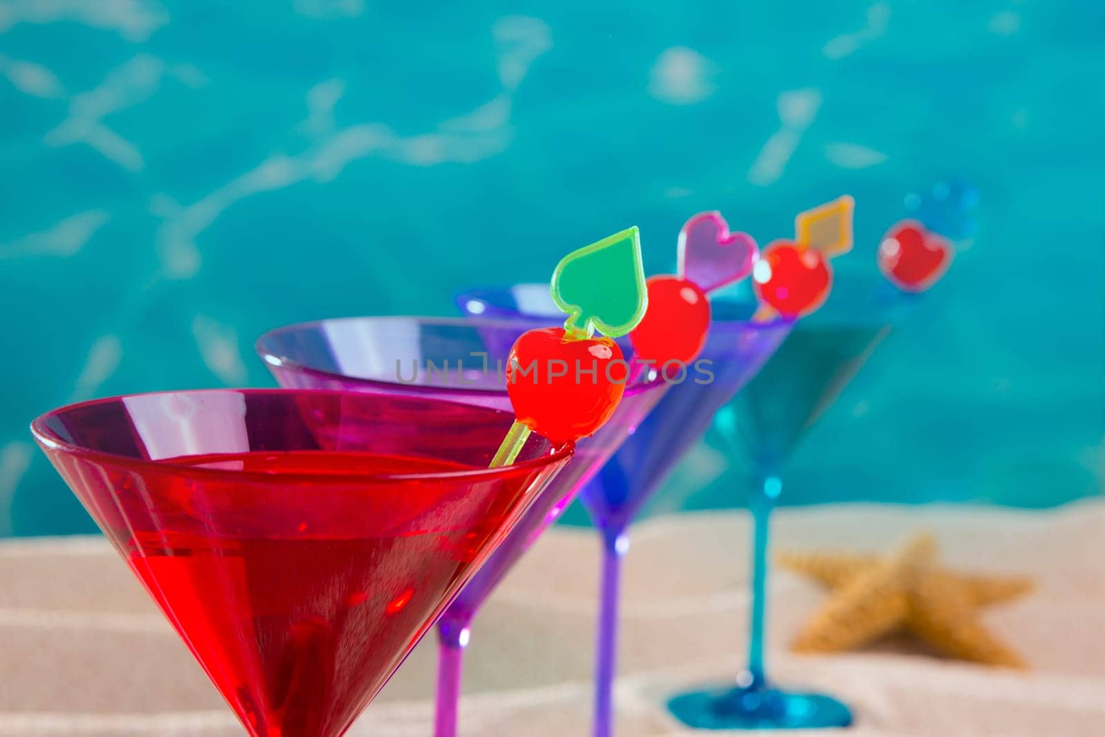 colorful cocktail in a row with cherry on tropical sand beach of turquoise sea