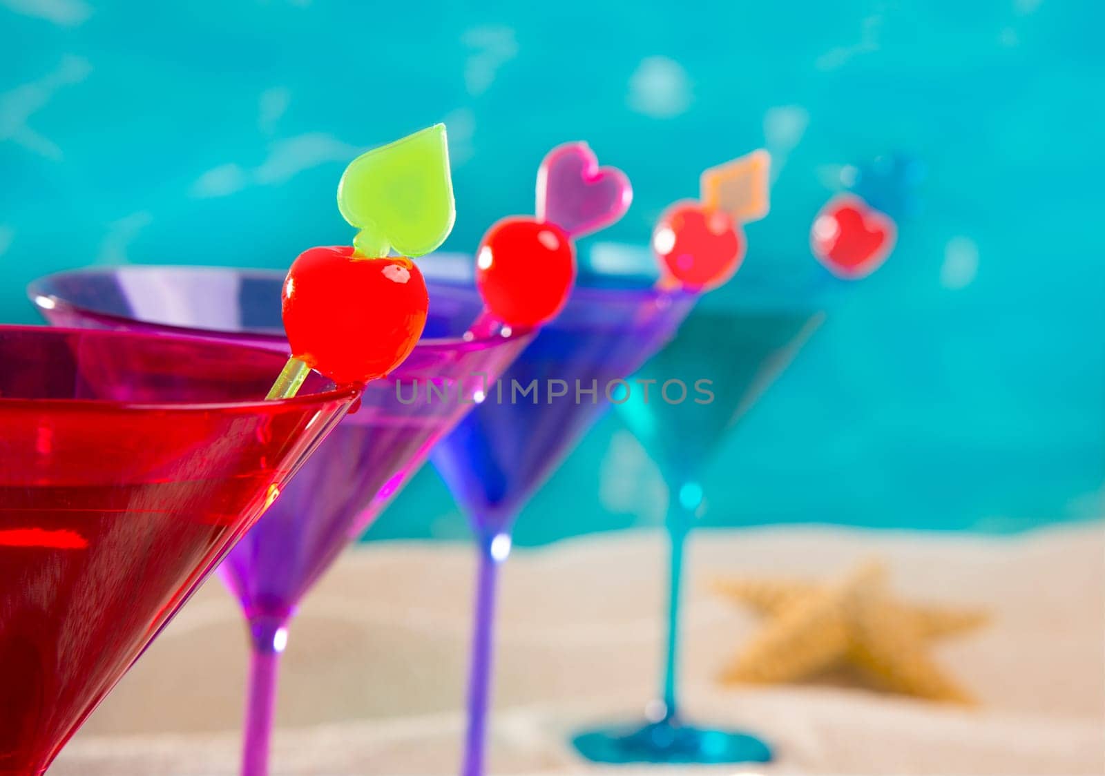 colorful cocktail in a row with cherry on tropical sand beach of turquoise sea