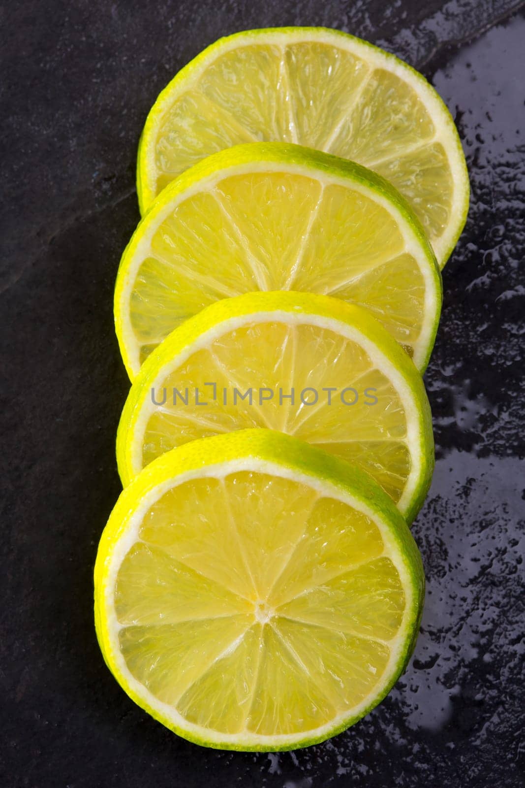 Fresh lima slices with water drops on black slate stone background