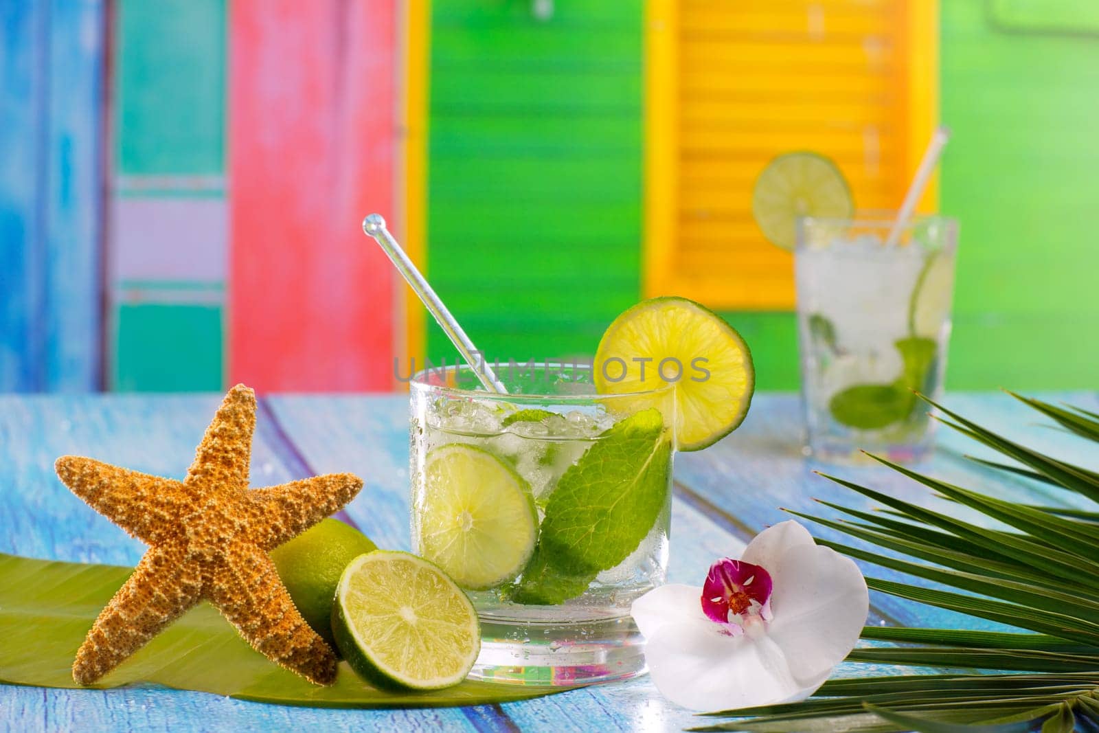 Cuban Mojito cocktail in tropical colorful house on blue wood with flowers and starfish