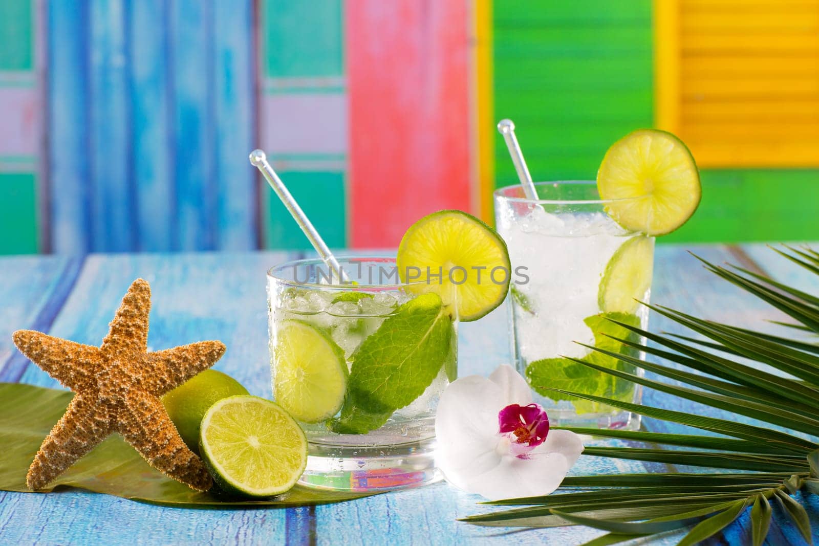 Cuban Mojito cocktail in tropical colorful house on blue wood with flowers and starfish