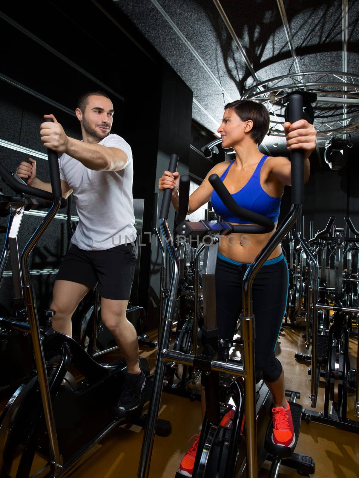 elliptical walker trainer man and woman at black gym training aerobics exercise