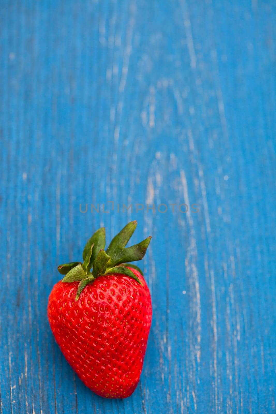 Closeup of one large fresh strawberry against light blue wooden background