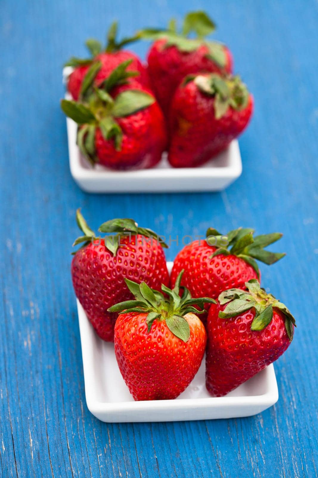 Closeup of large fresh strawberries in two white dishes on light blue wooden background
