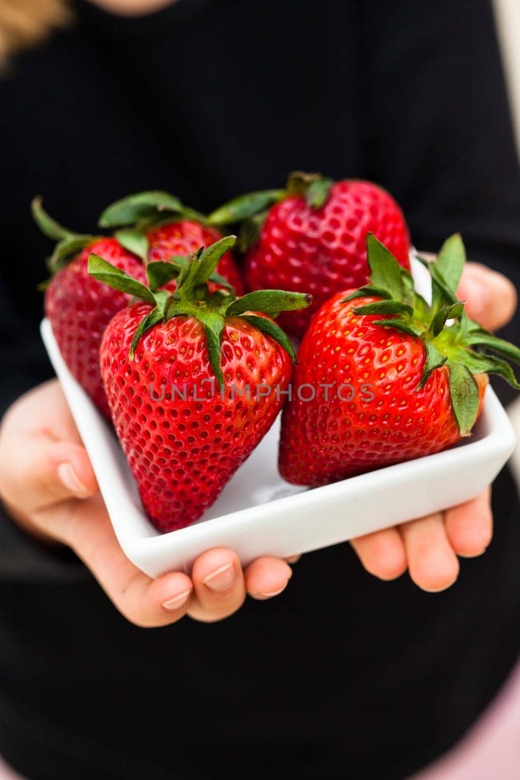 Closeup of four large fresh strawberries in white dish being held in hands of young child