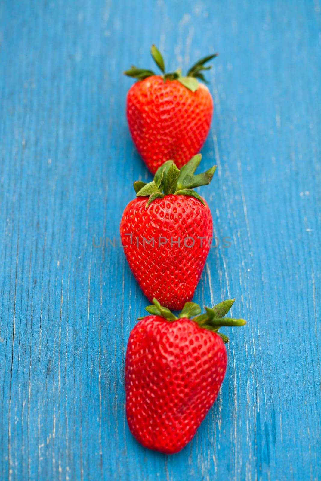Closeup of three large fresh strawberries in row against light blue wooden background