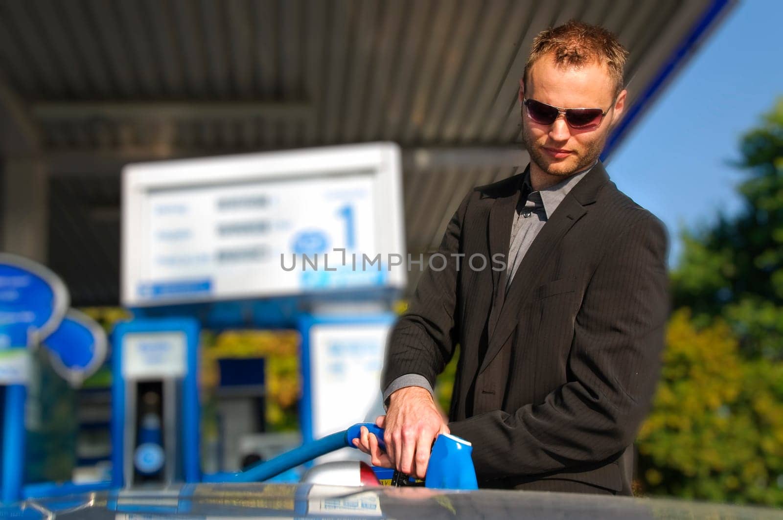 Young man in a dark suit standing at the gas station and filled up his silver sports car