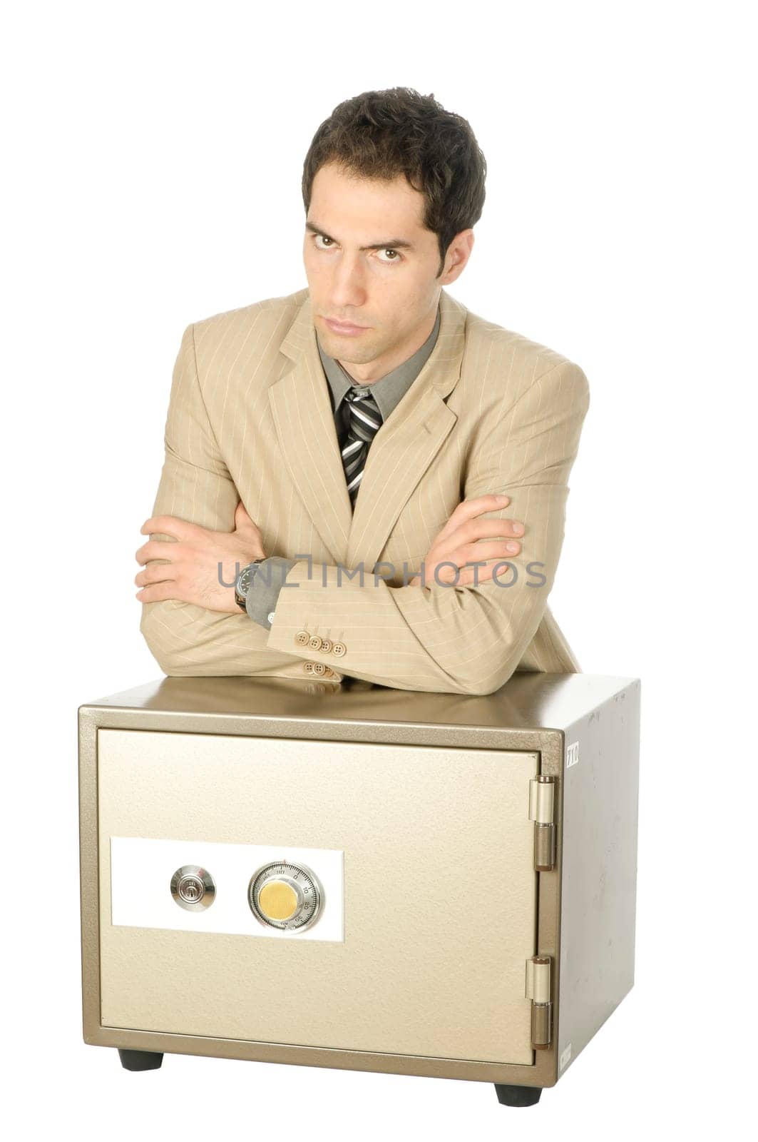 Young male businessman in light suit stands with his arms folded behind a locked safe, isolated against white background.