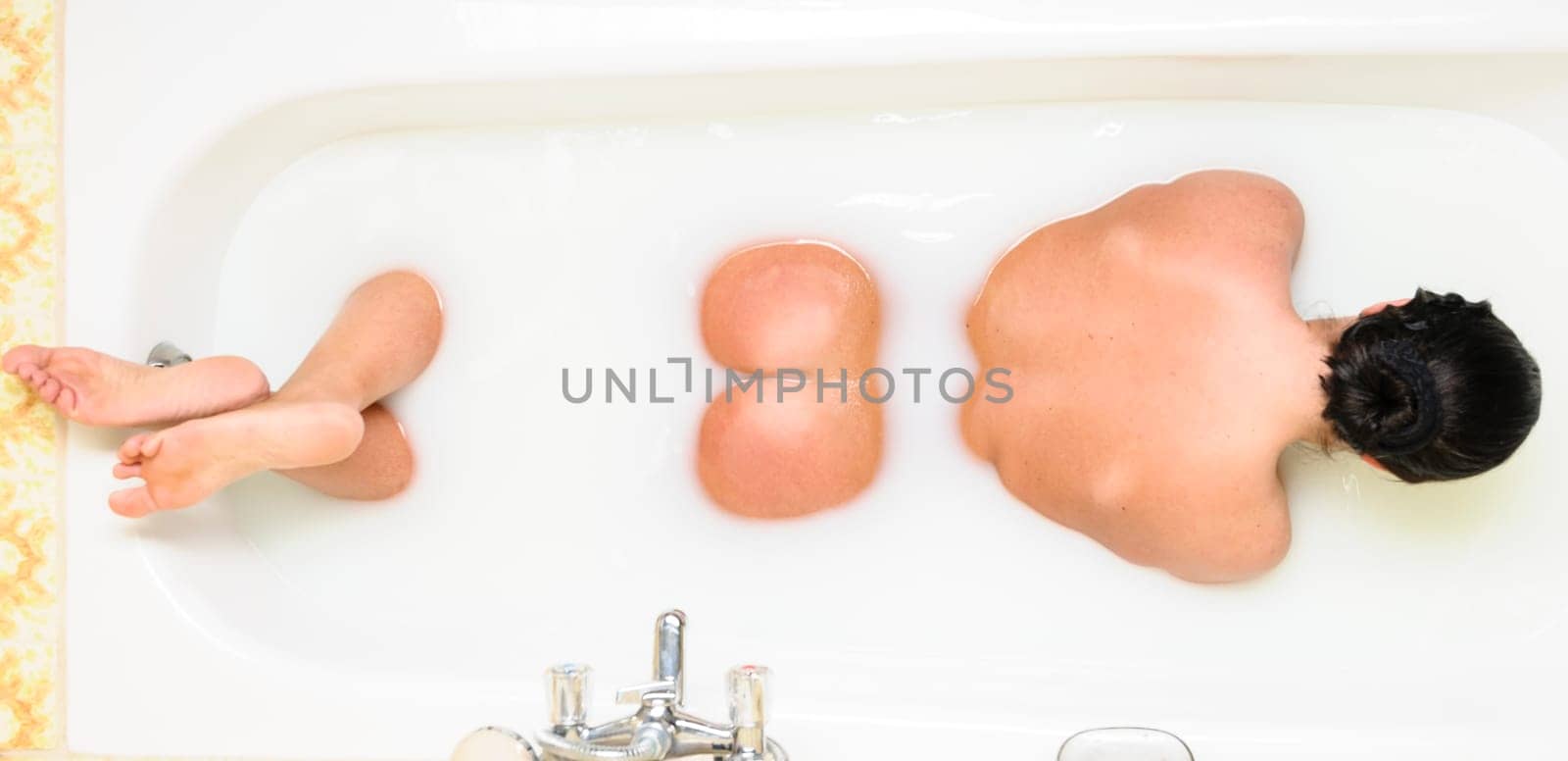 Adult woman lying in the bath showing her backsite.