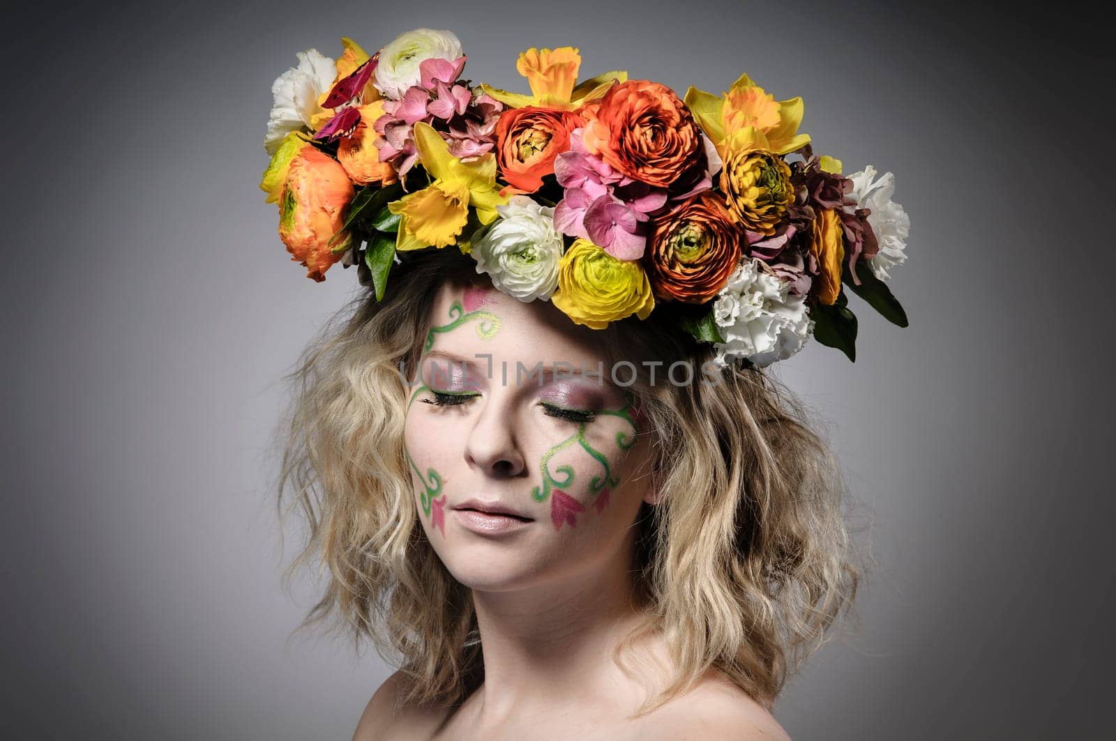Spring portrait of a young woman with spring-like make-up and a colorful flower wreath in her hair.