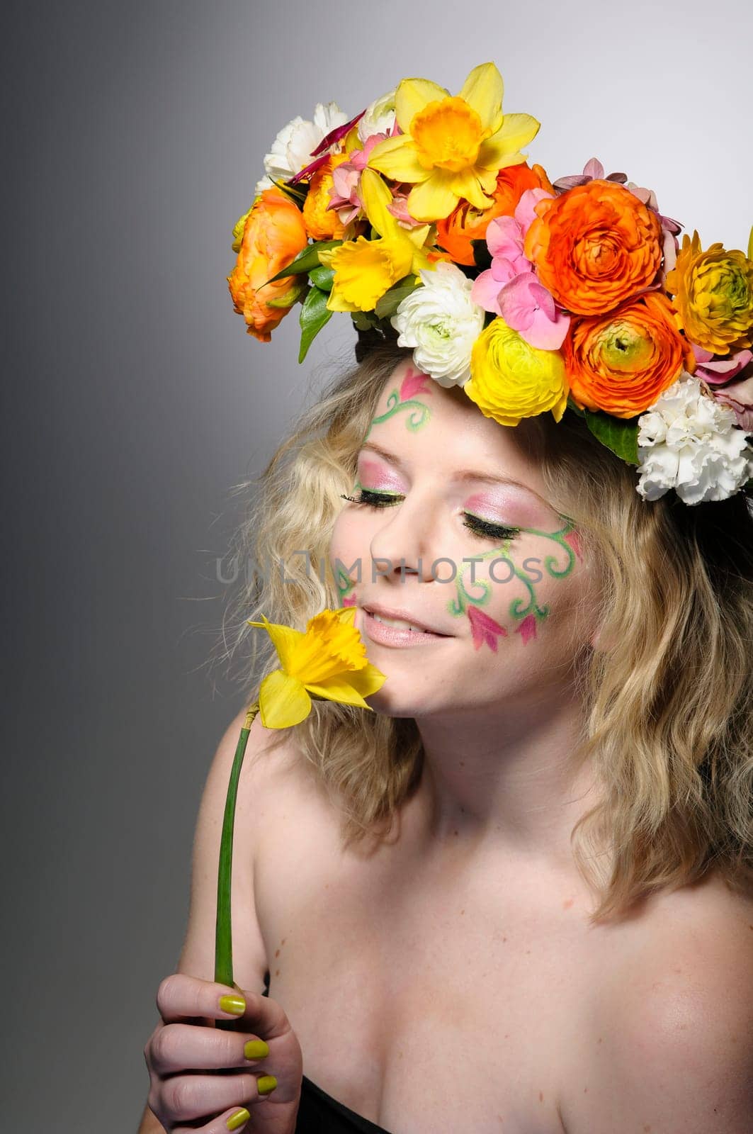 Spring portrait of a young woman with spring-like make-up and a colorful flower wreath in her hair.