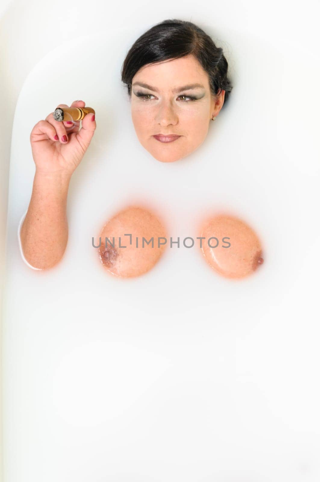 Adult woman lying in the bath with delight when and smokes a big cigar