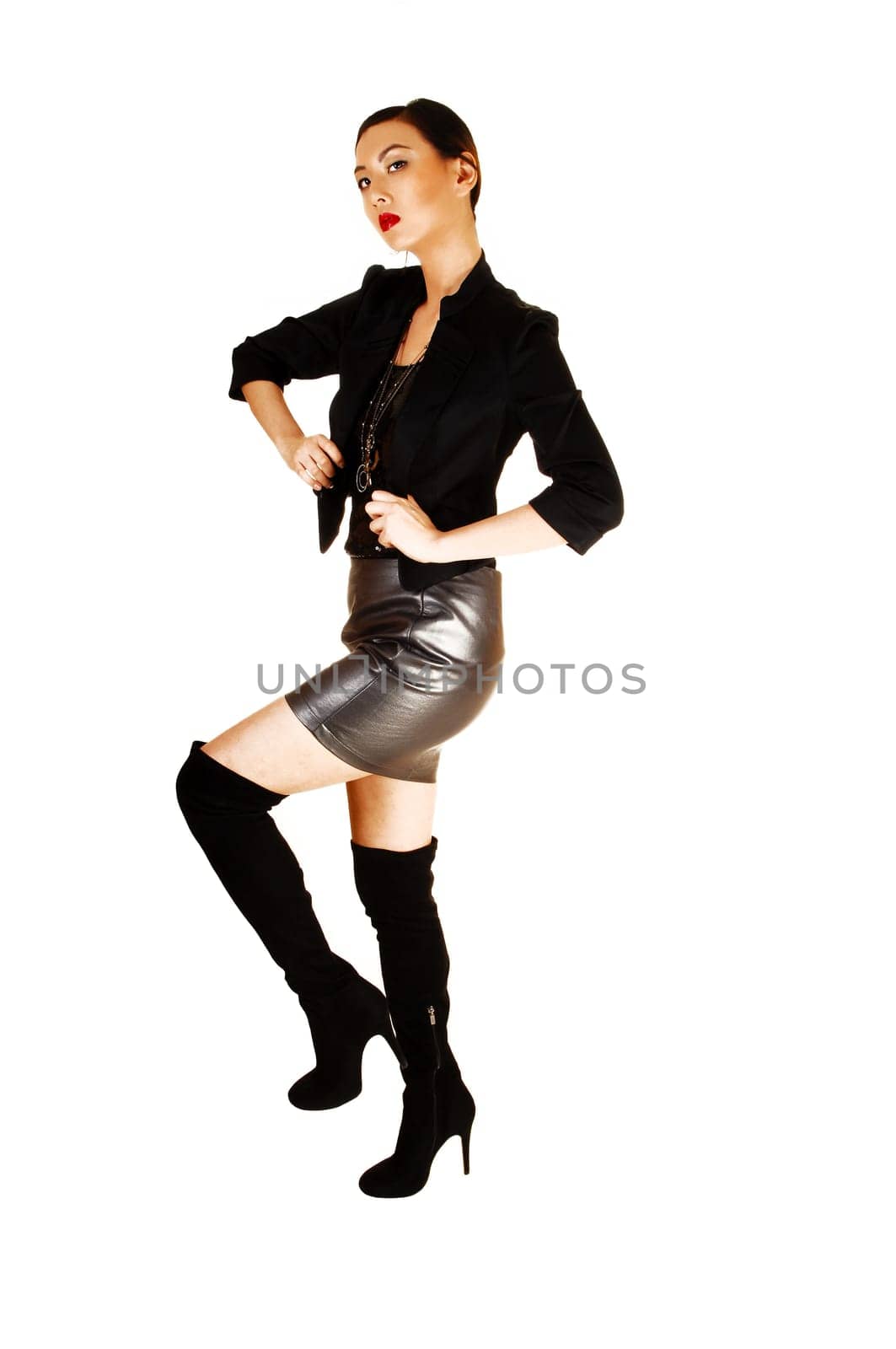 A young pretty slim chinese woman in a black blouse and light jacket and gray leather skirt and long black boots, standing for white background.