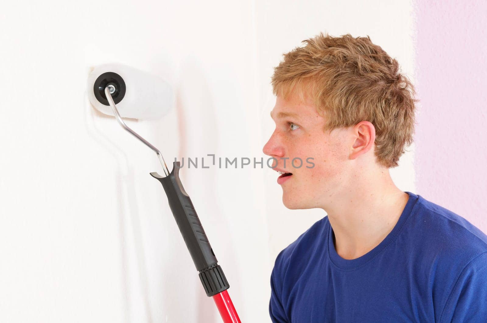 Young man in a T-shirt paints the walls of his first apartment in bright colors.