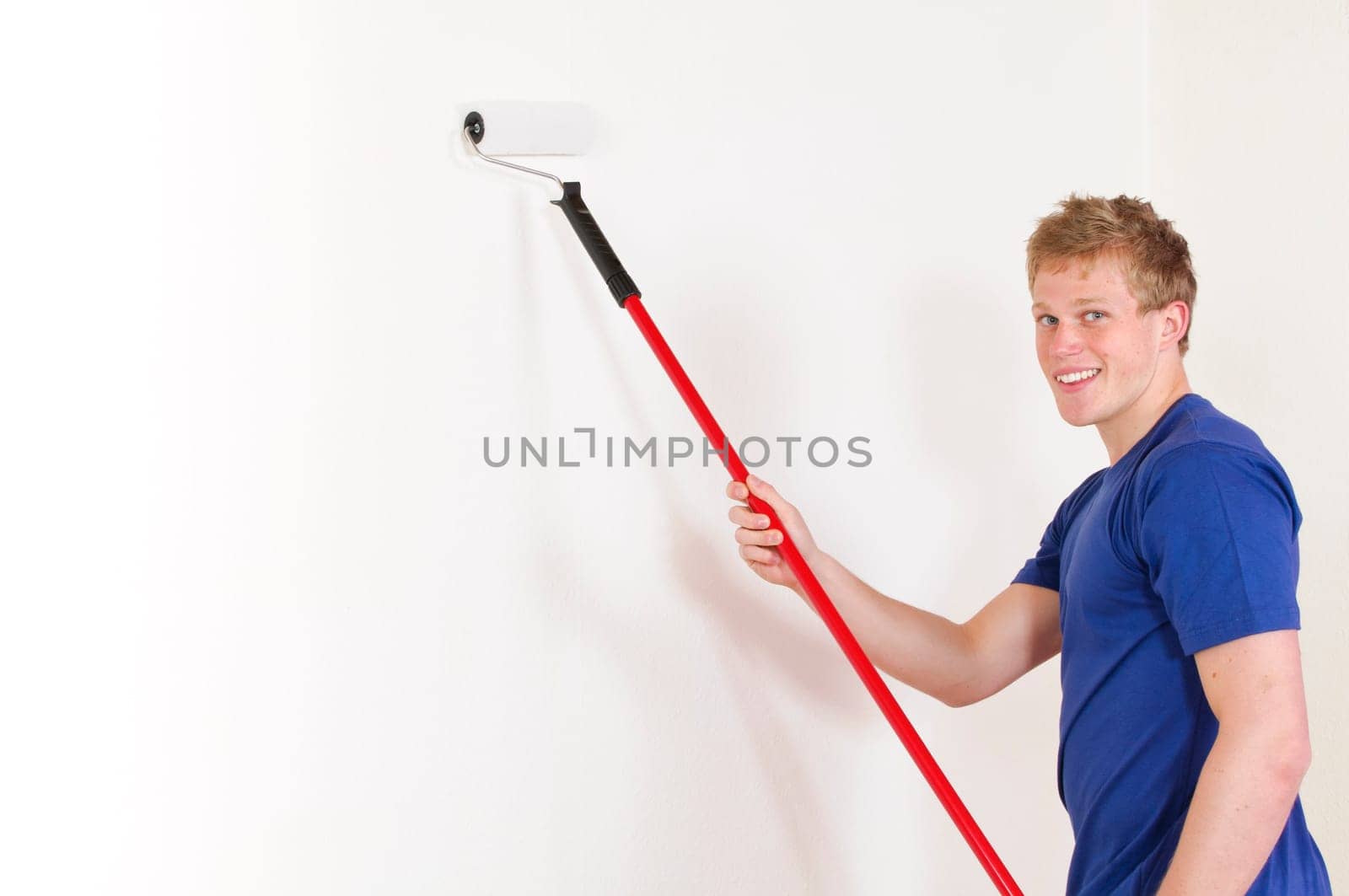 Young man in a T-shirt paints the walls of his first apartment in bright colors.