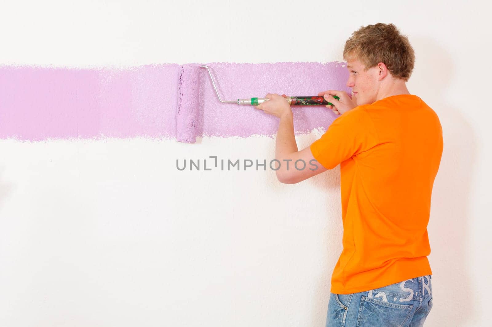 Young man in a T-shirt paints the walls of his first apartment in bright colors.