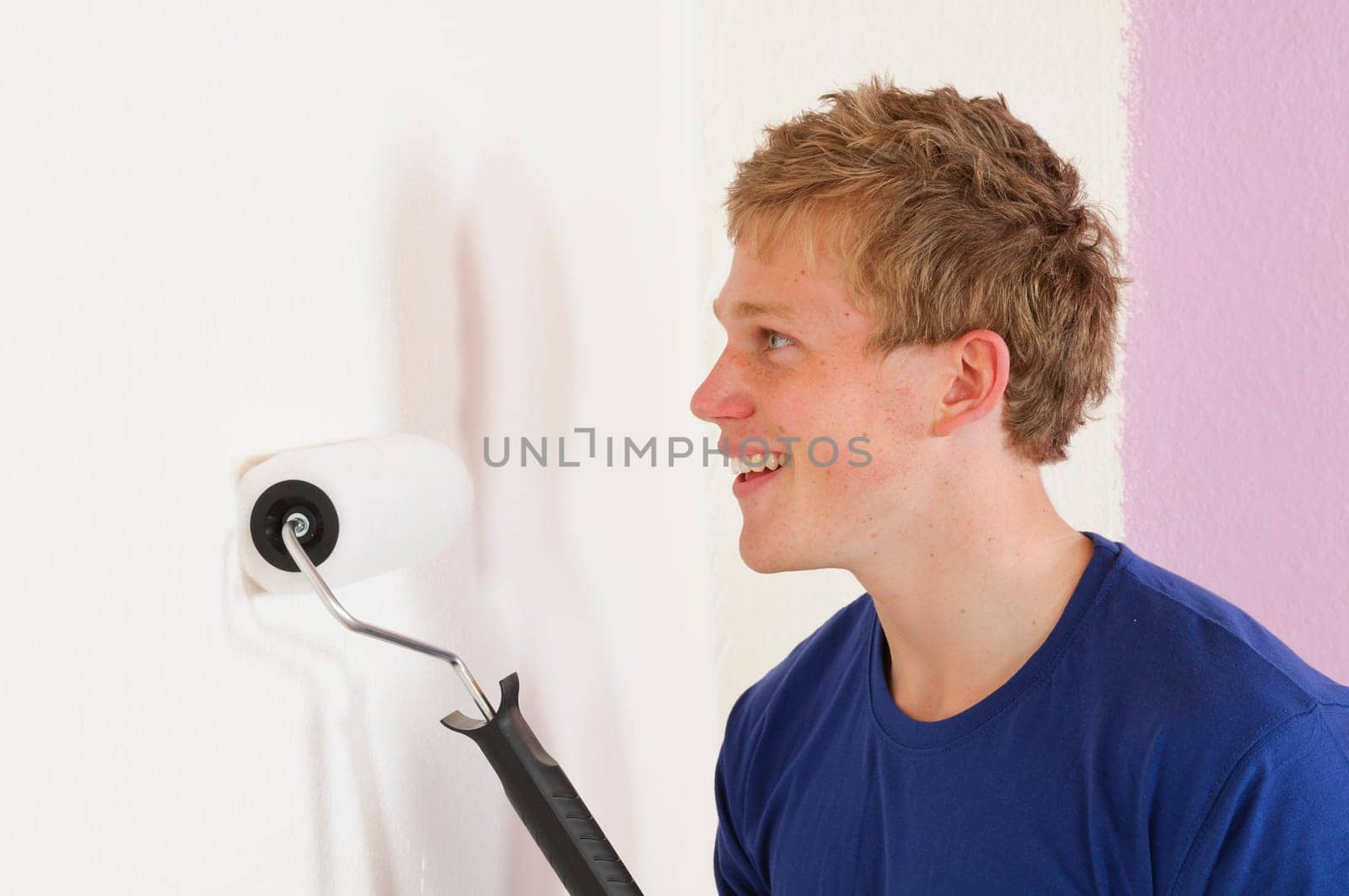 Young man in a T-shirt paints the walls of his first apartment in bright colors.