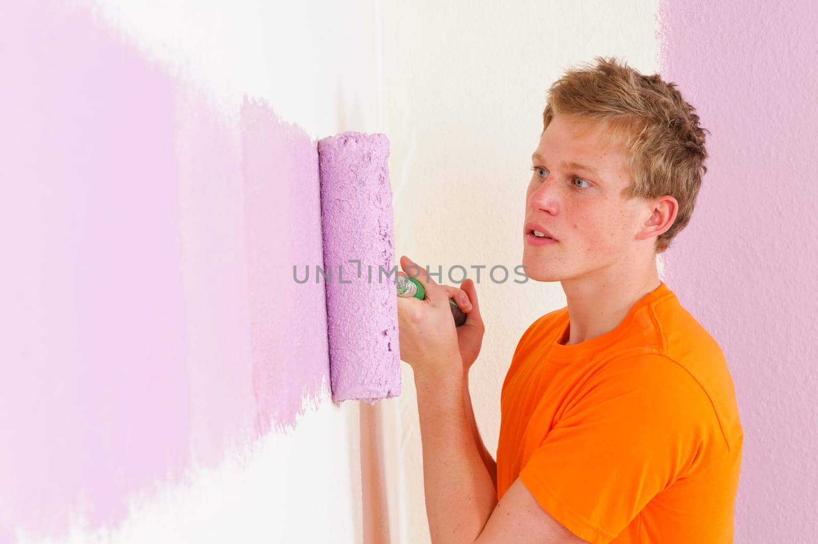 Young man in a T-shirt paints the walls of his first apartment in bright colors.
