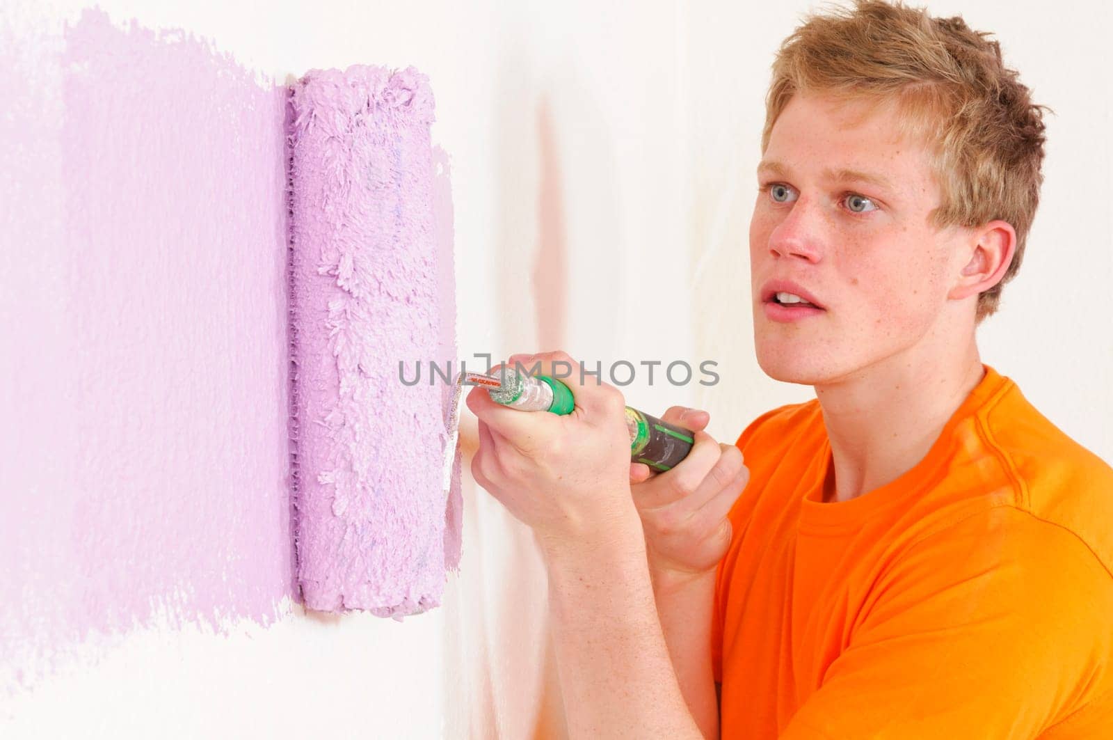 Young man in a T-shirt paints the walls of his first apartment in bright colors.