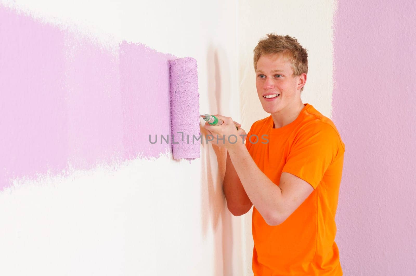 Young man in a T-shirt paints the walls of his first apartment in bright colors.