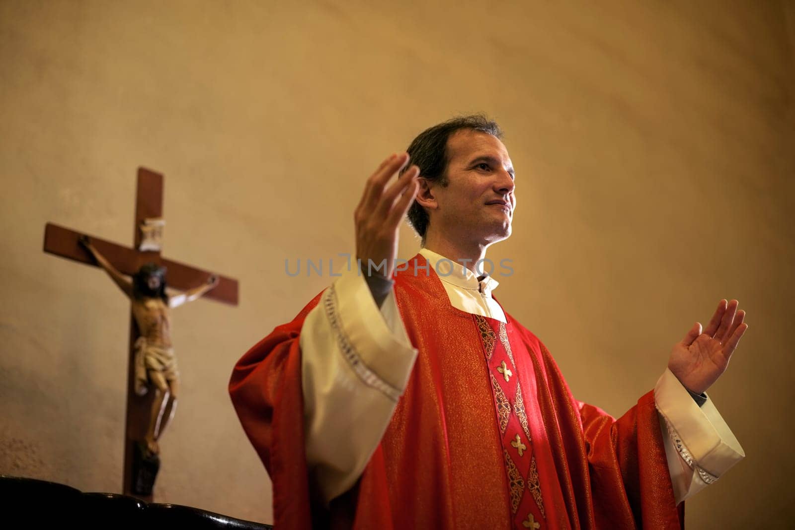 Catholic priest on altar praying with open arms during mass service in church