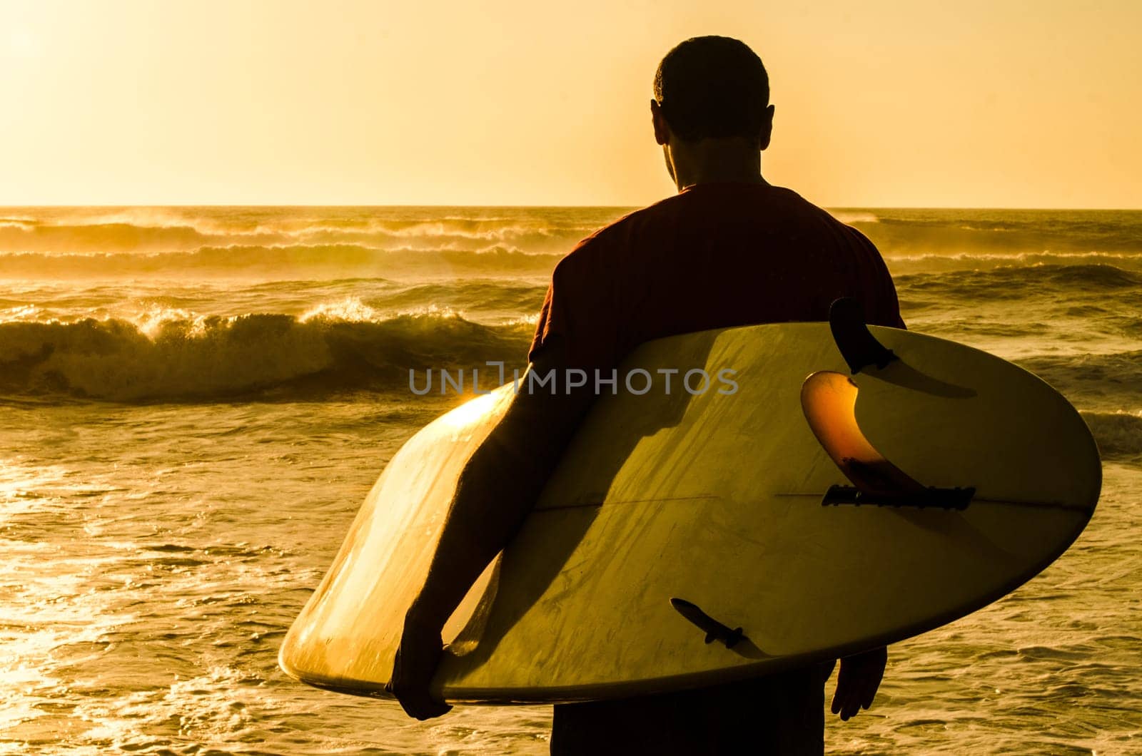 A surfer watching the waves at sunset in Portugal.