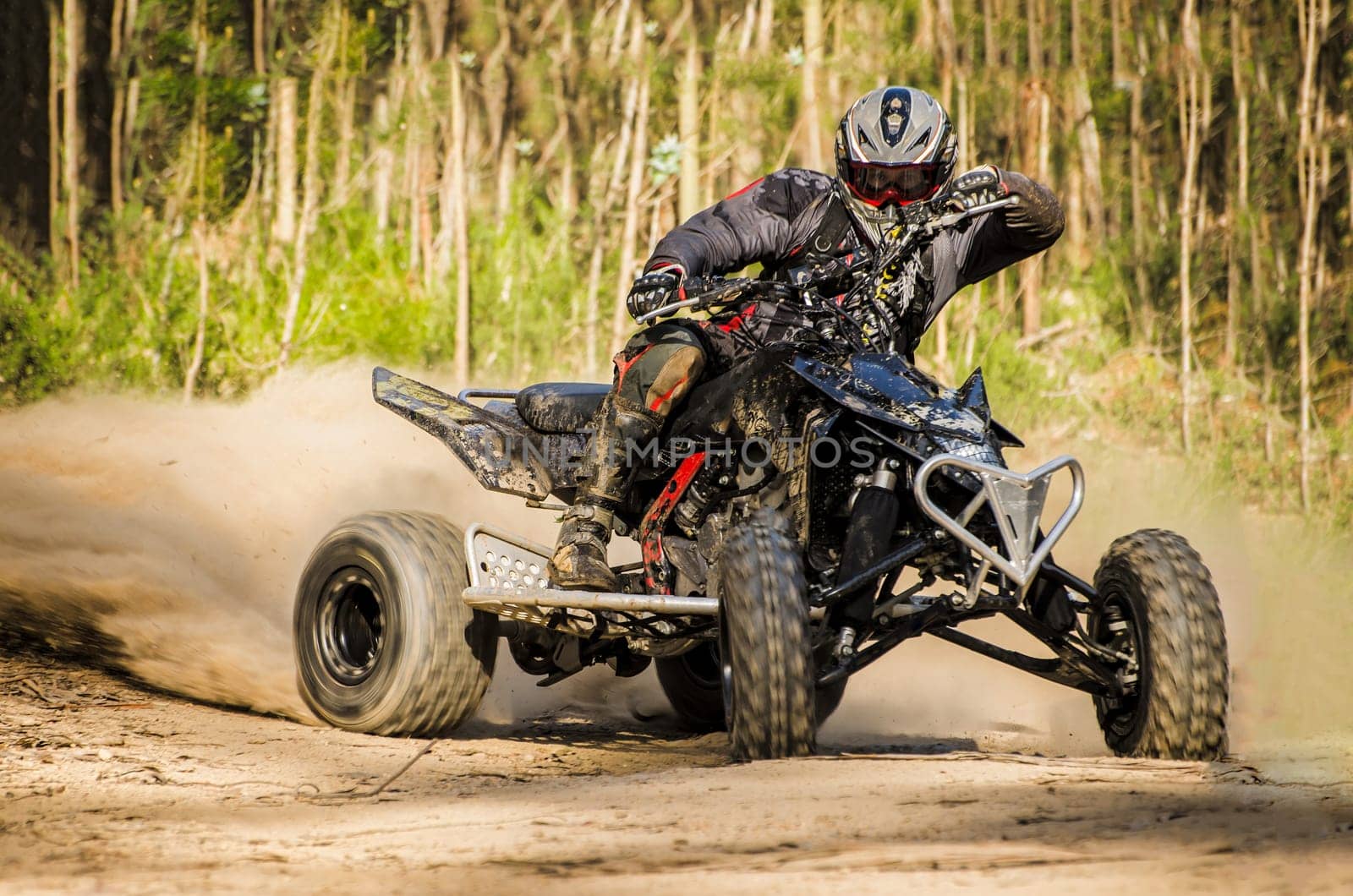 ATV racer takes a turn during a race on a dusty terrain.