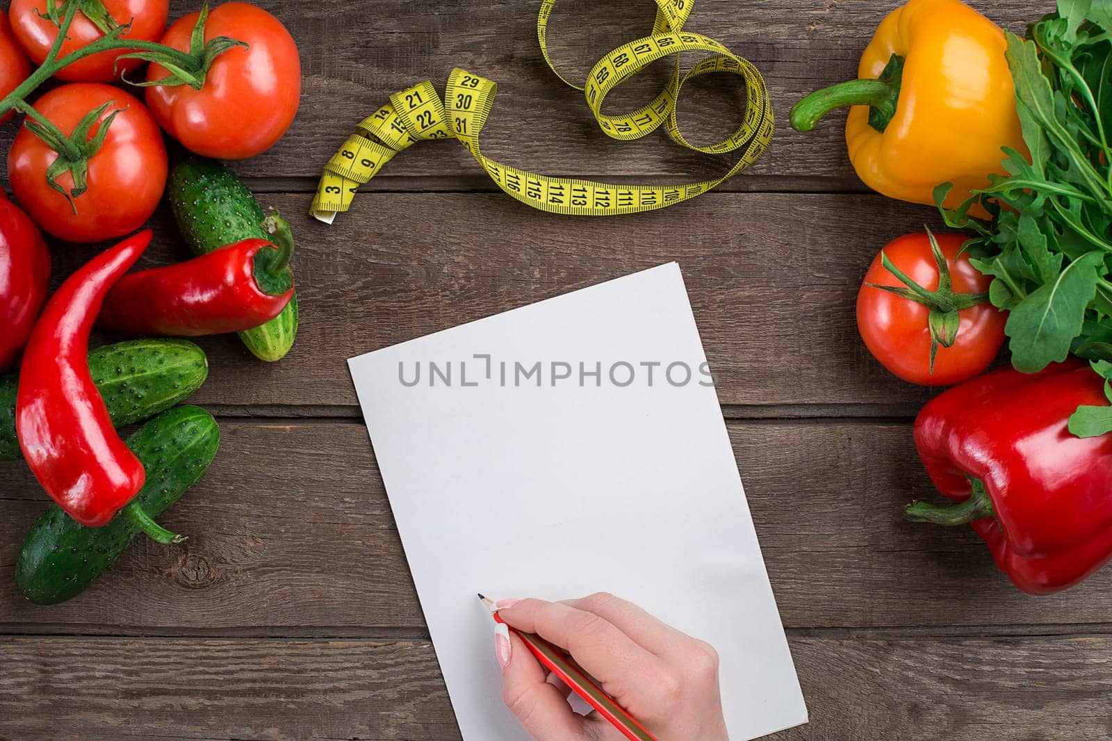 Concept diet, slimming plan with vegetables top view mock up. A female hand in a sports bracelet writes an article about proper nutrition