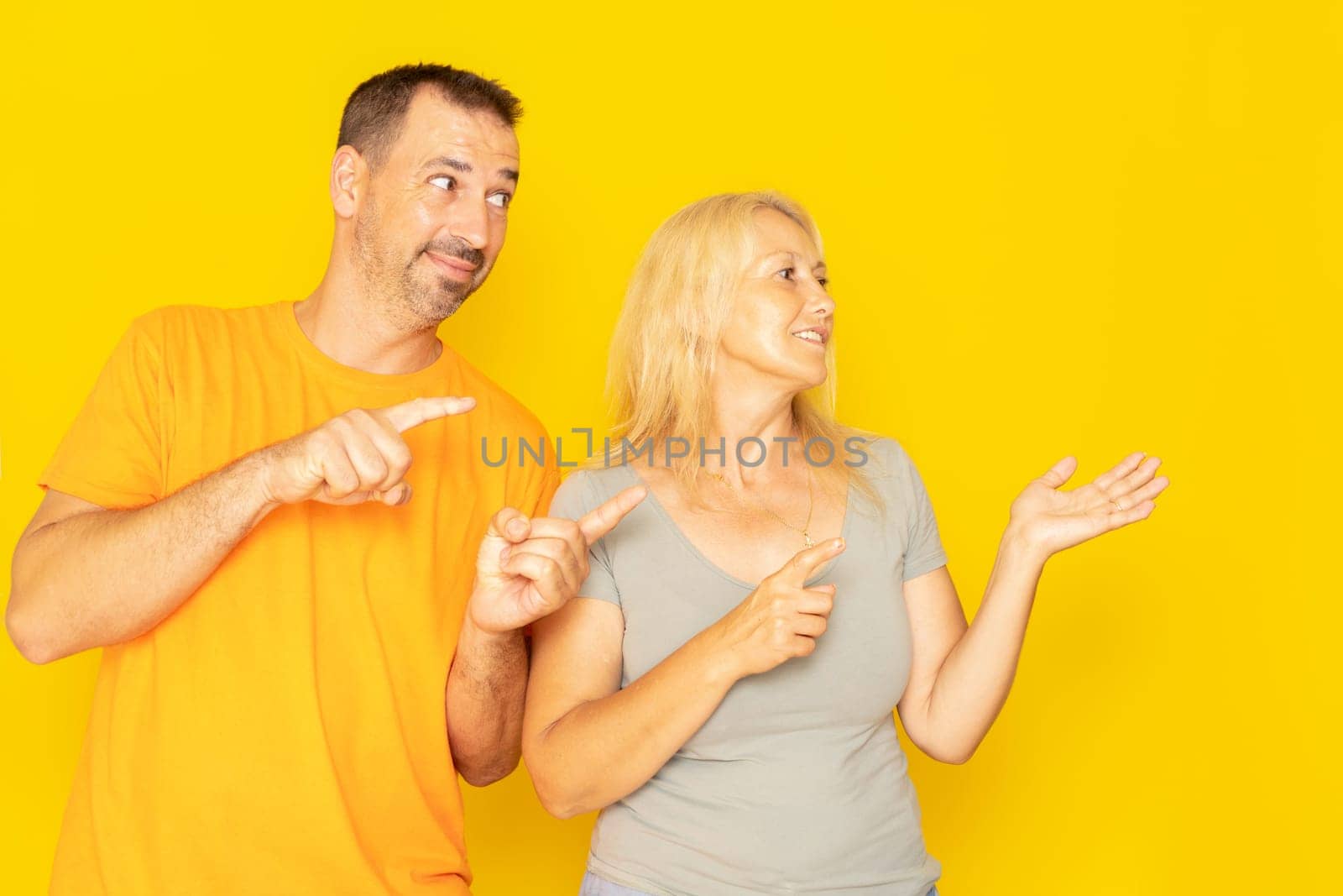 Beautiful caucasian couple in their 40s dressed in casual clothes smiling and looking at the camera pointing with two hands and fingers to the side.