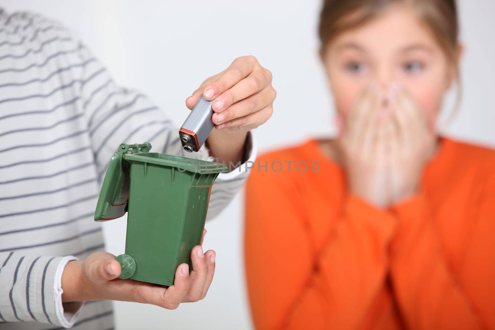 Closeup of a boy putting a battery in a miniature bin much to the horror of his sister