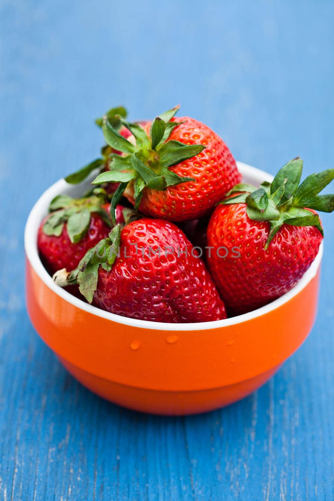 Closeup of large fresh strawberries in orange bowl against light blue background