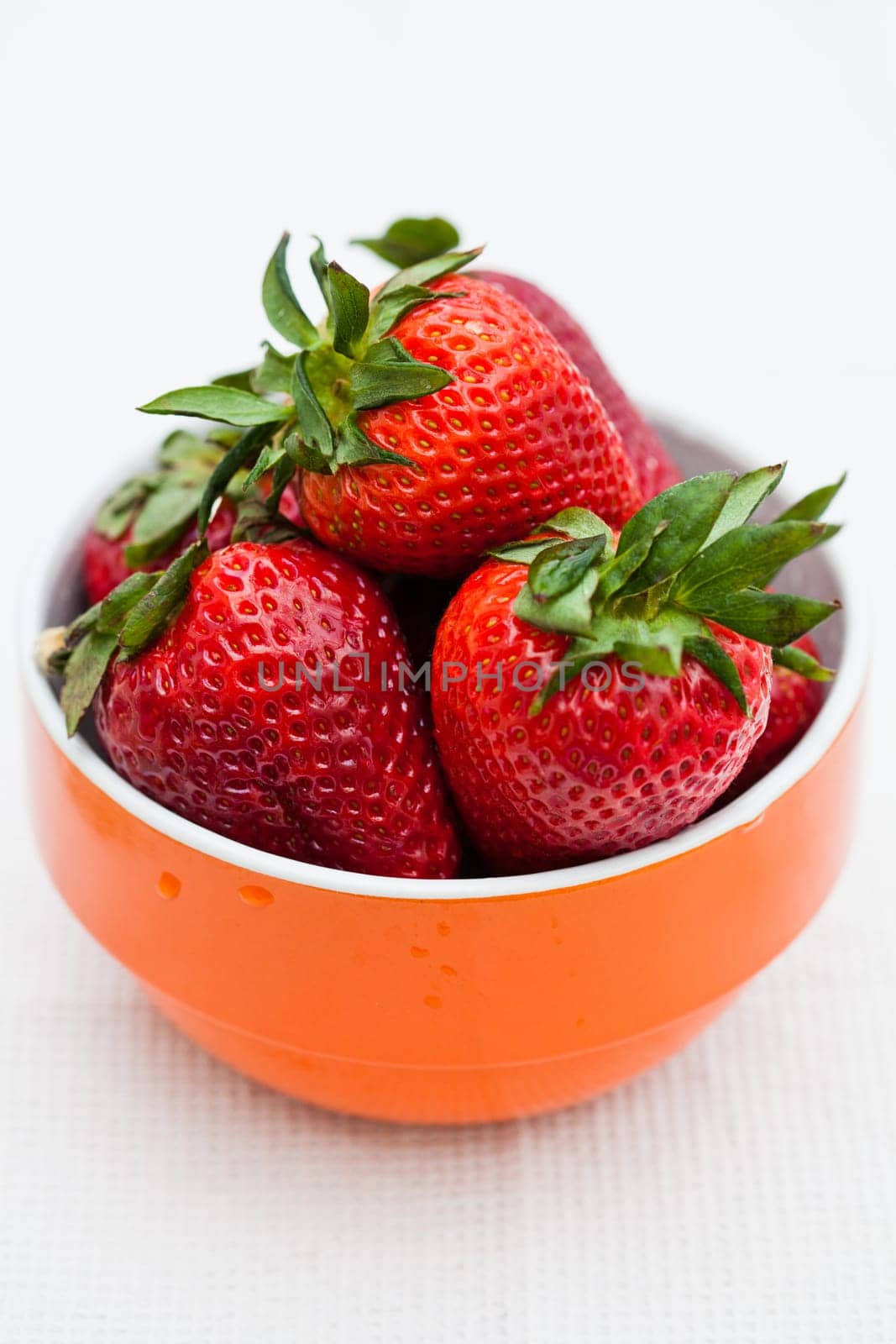 Closeup of large fresh strawberries in orange bowl against light background