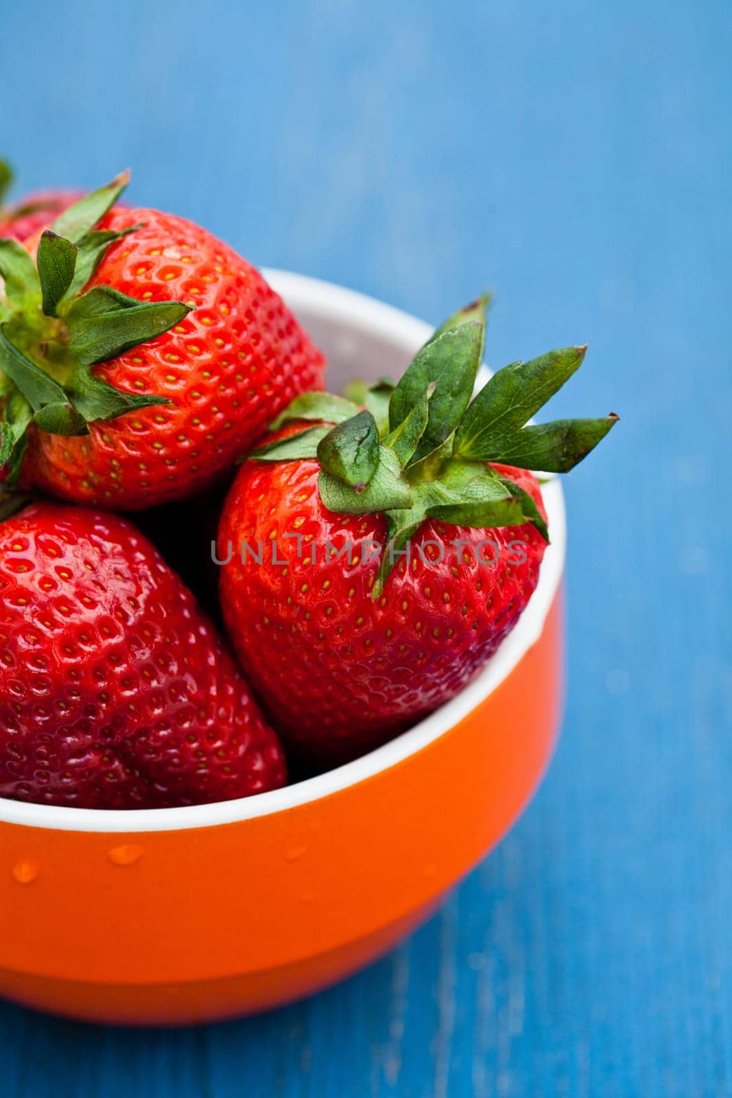 Closeup of large fresh strawberries in orange bowl against light blue background