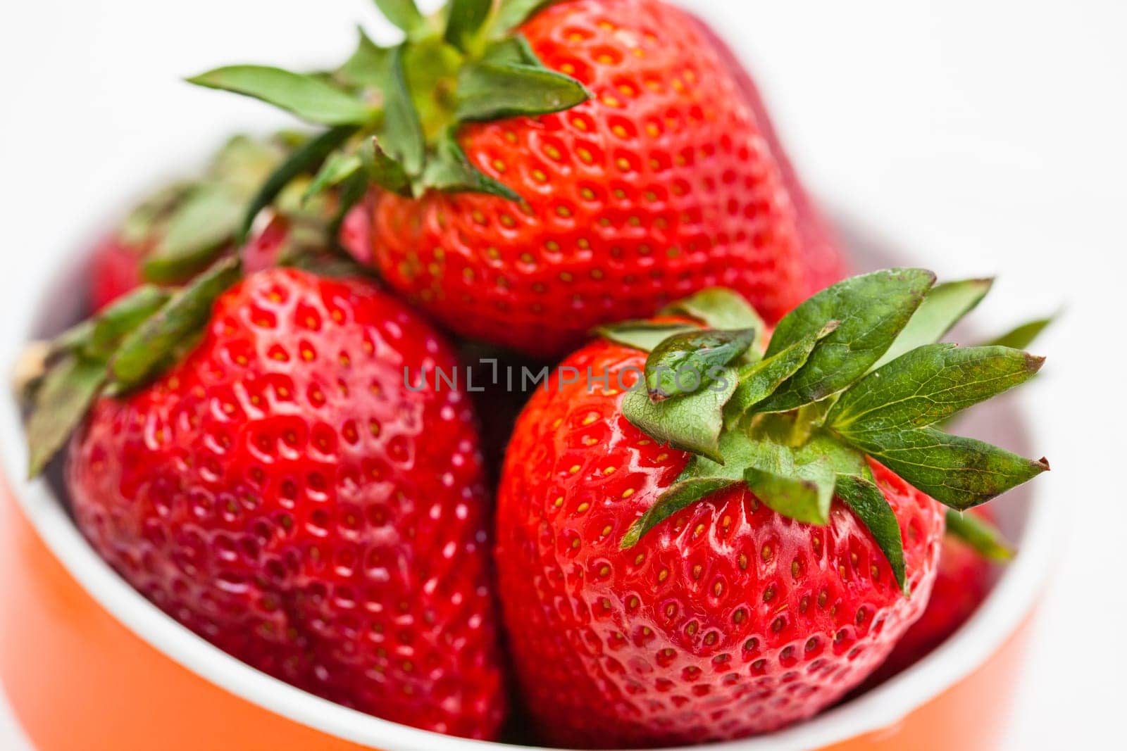 Closeup of large fresh strawberries in orange bowl against light background