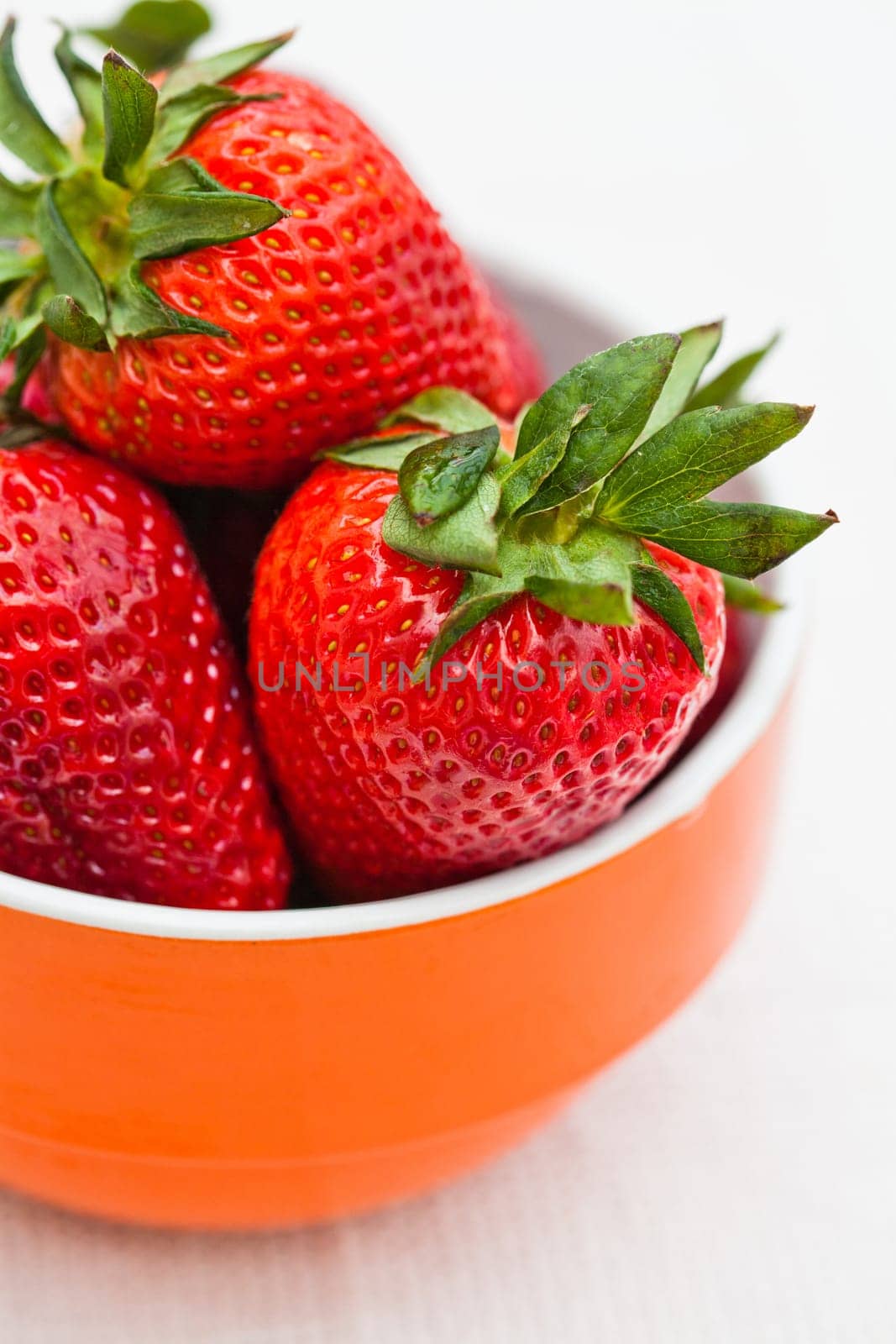 Closeup of large fresh strawberries in orange bowl against light background