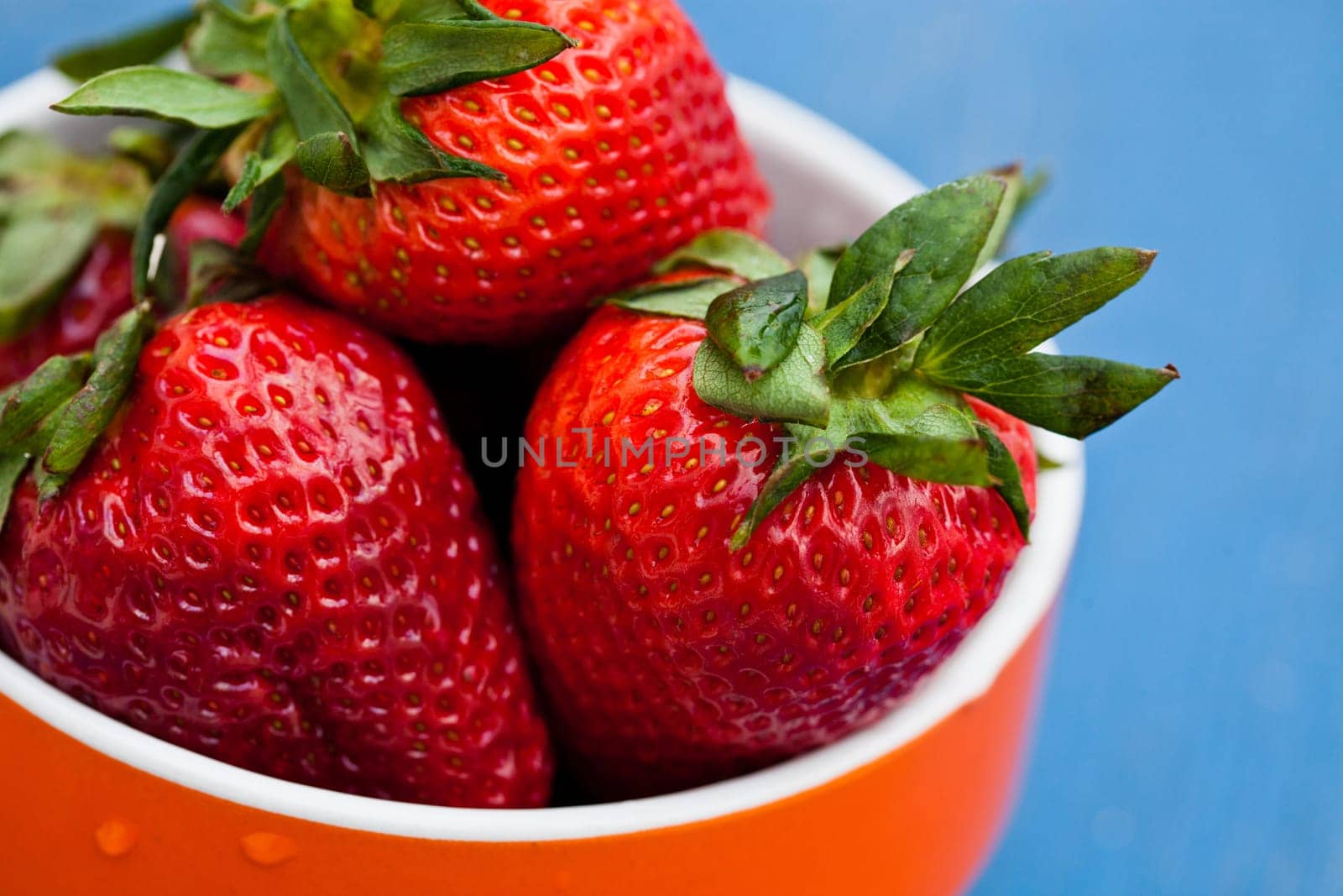 Closeup of large fresh strawberries in orange bowl against light blue background