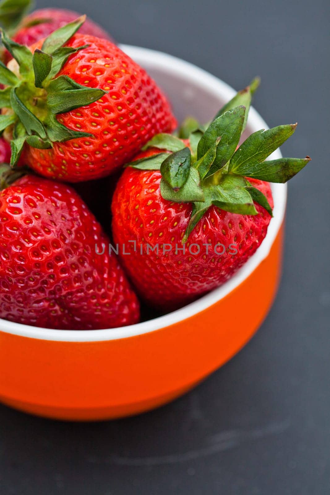 Closeup of large fresh strawberries in orange bowl against dark background