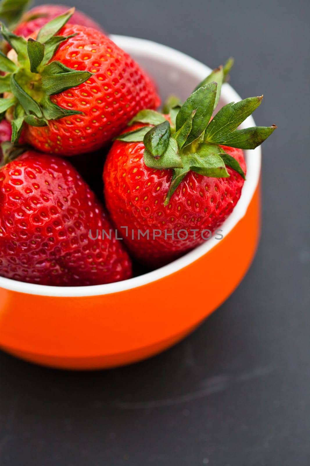 Closeup of large fresh strawberries in orange bowl against dark background