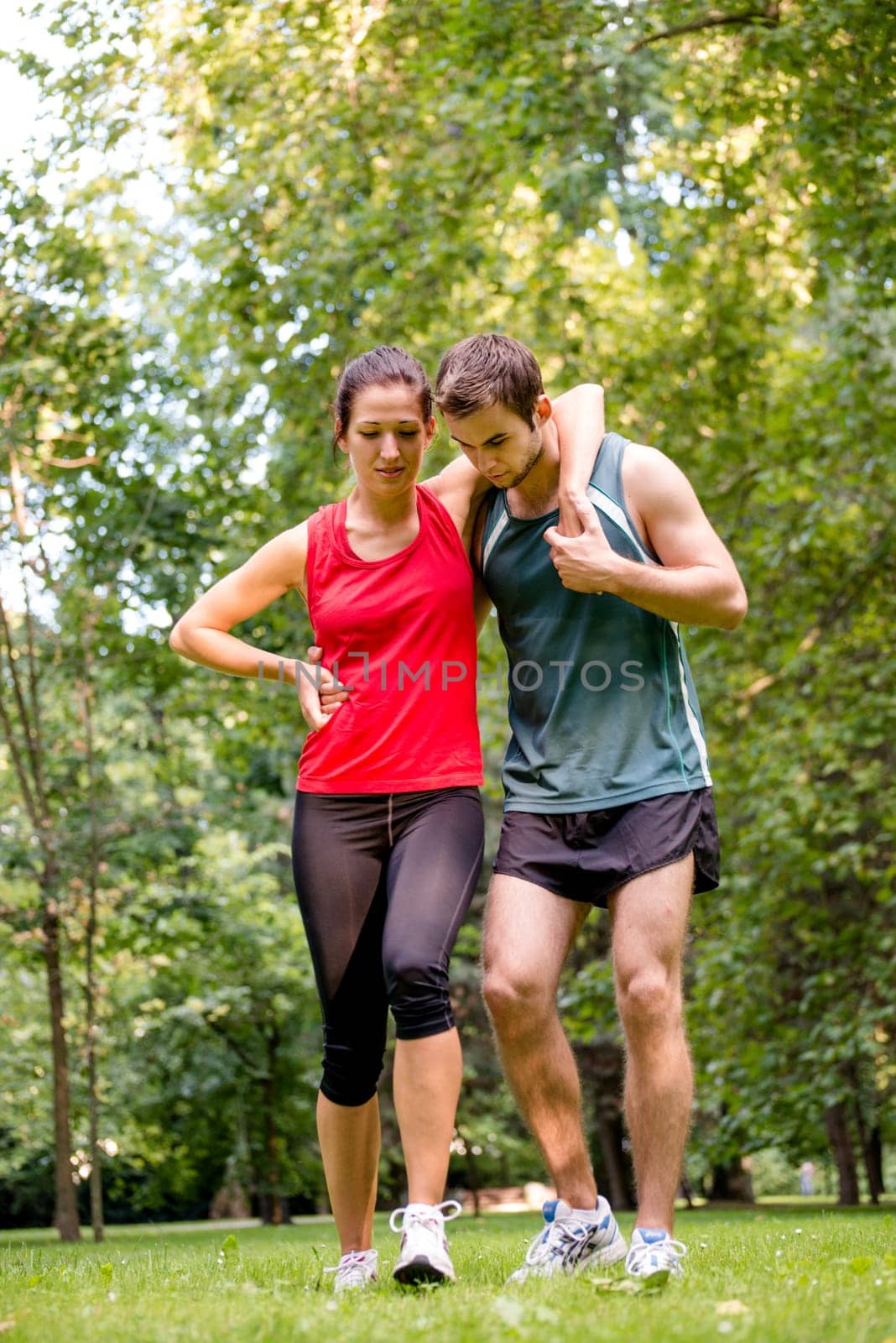 Sport injury - young fitness woman holding her ankle with pain, man is helping