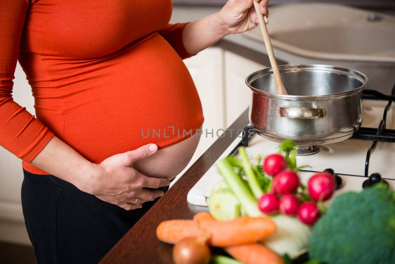 Crop of belly - pregnant woman cooking vegetables in kitchen