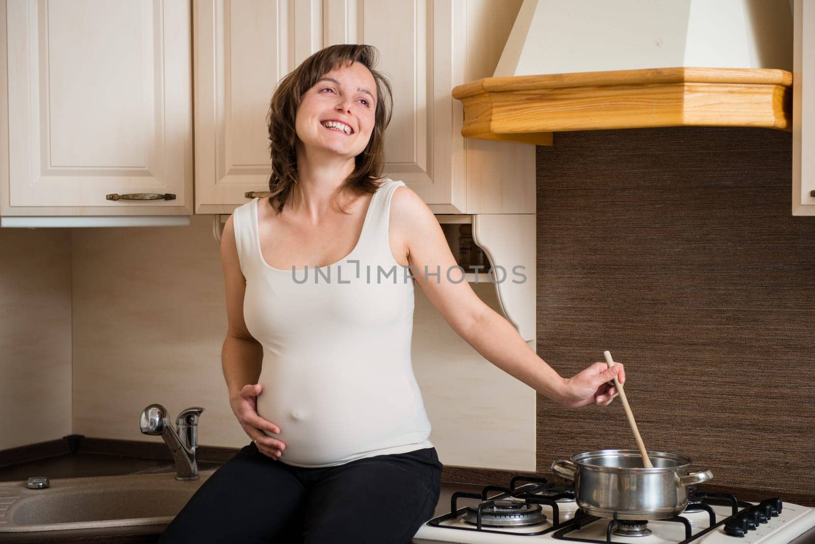 Lifestyle portrait of smiling pregnant woman cooking in home kitchen