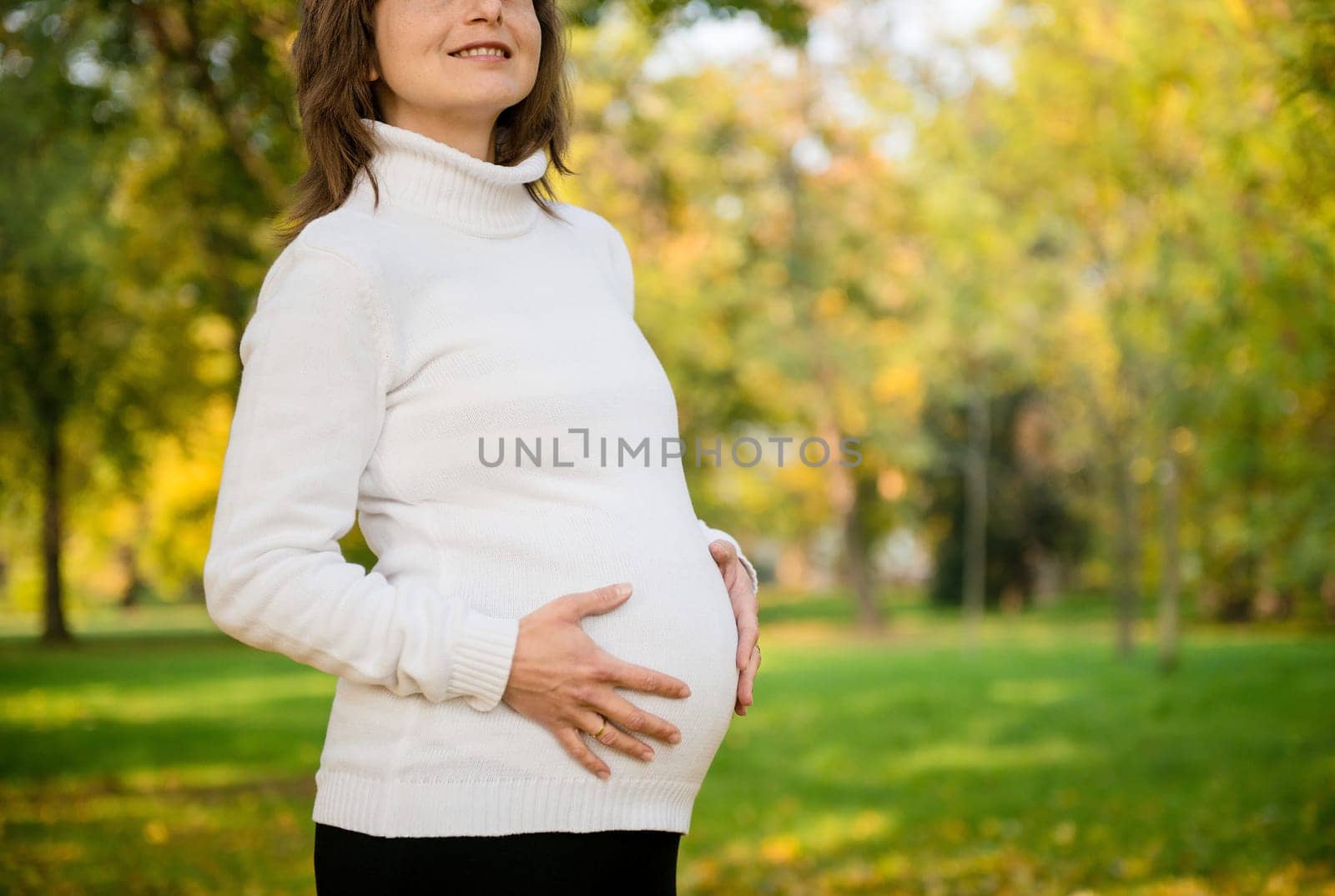 Detail of pregnant woman holding belly outdoor in nature