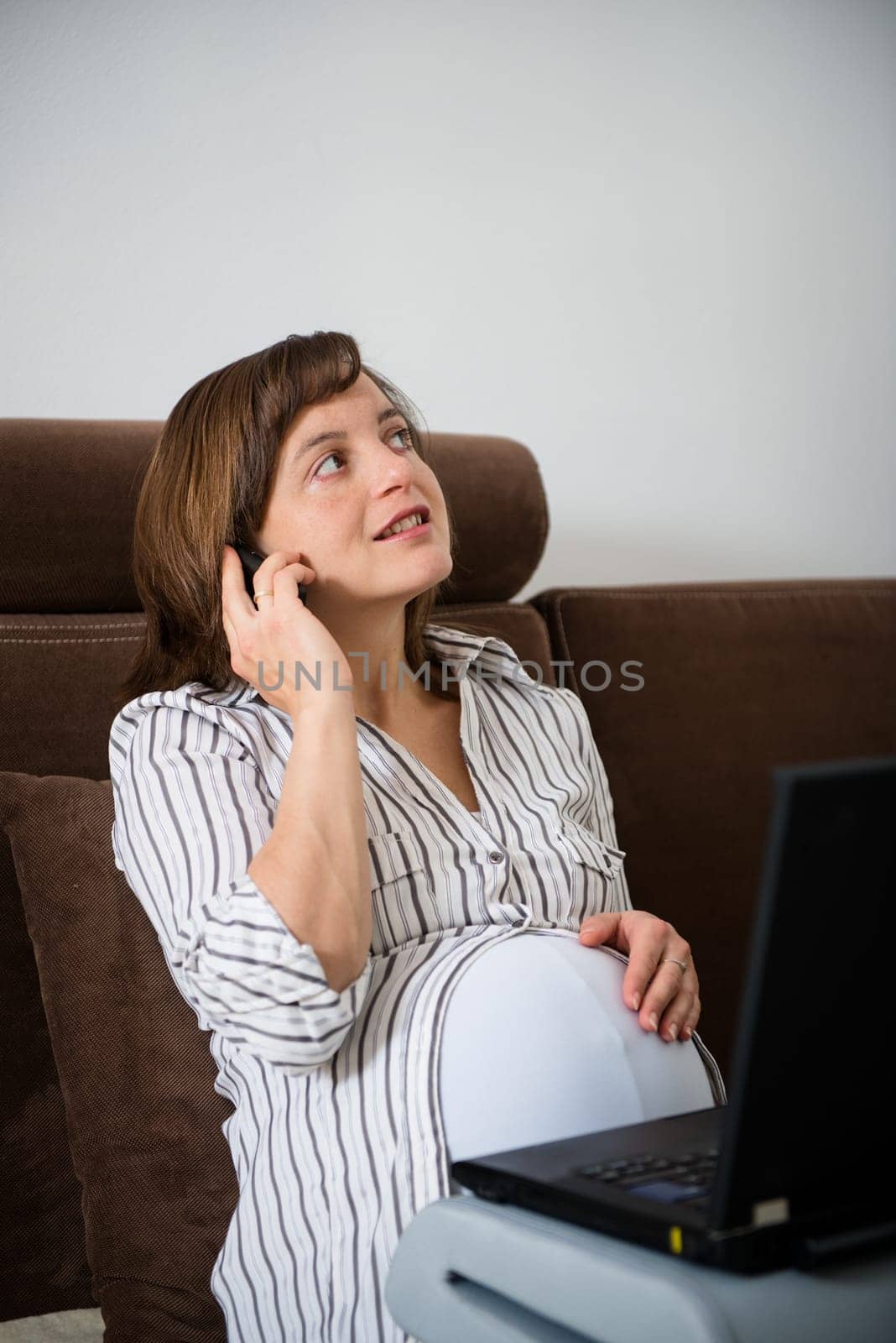Pregnant woman working on laptop from home and calling phone
