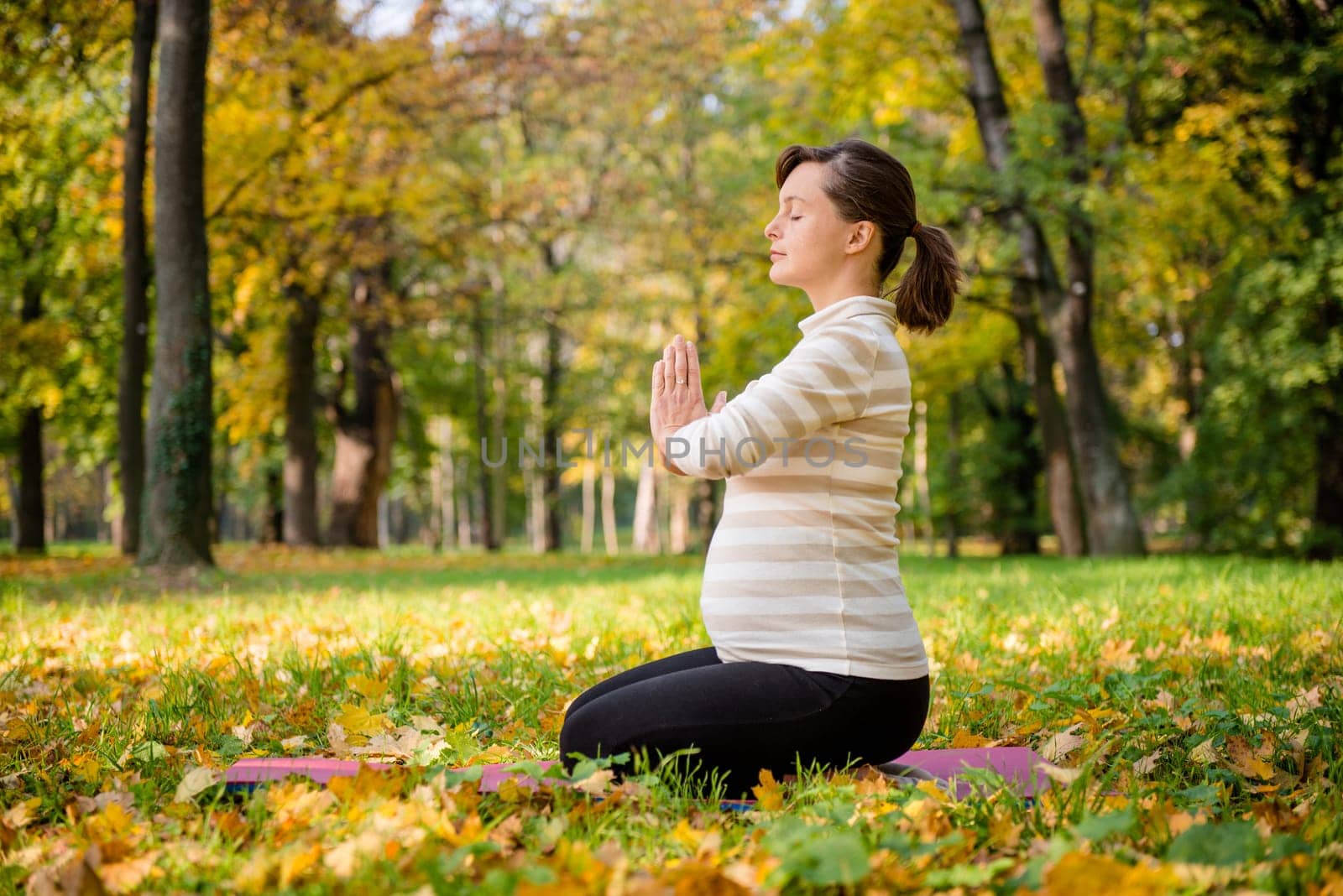 Young pregnant woman meditating outside in beautiful autumn nature