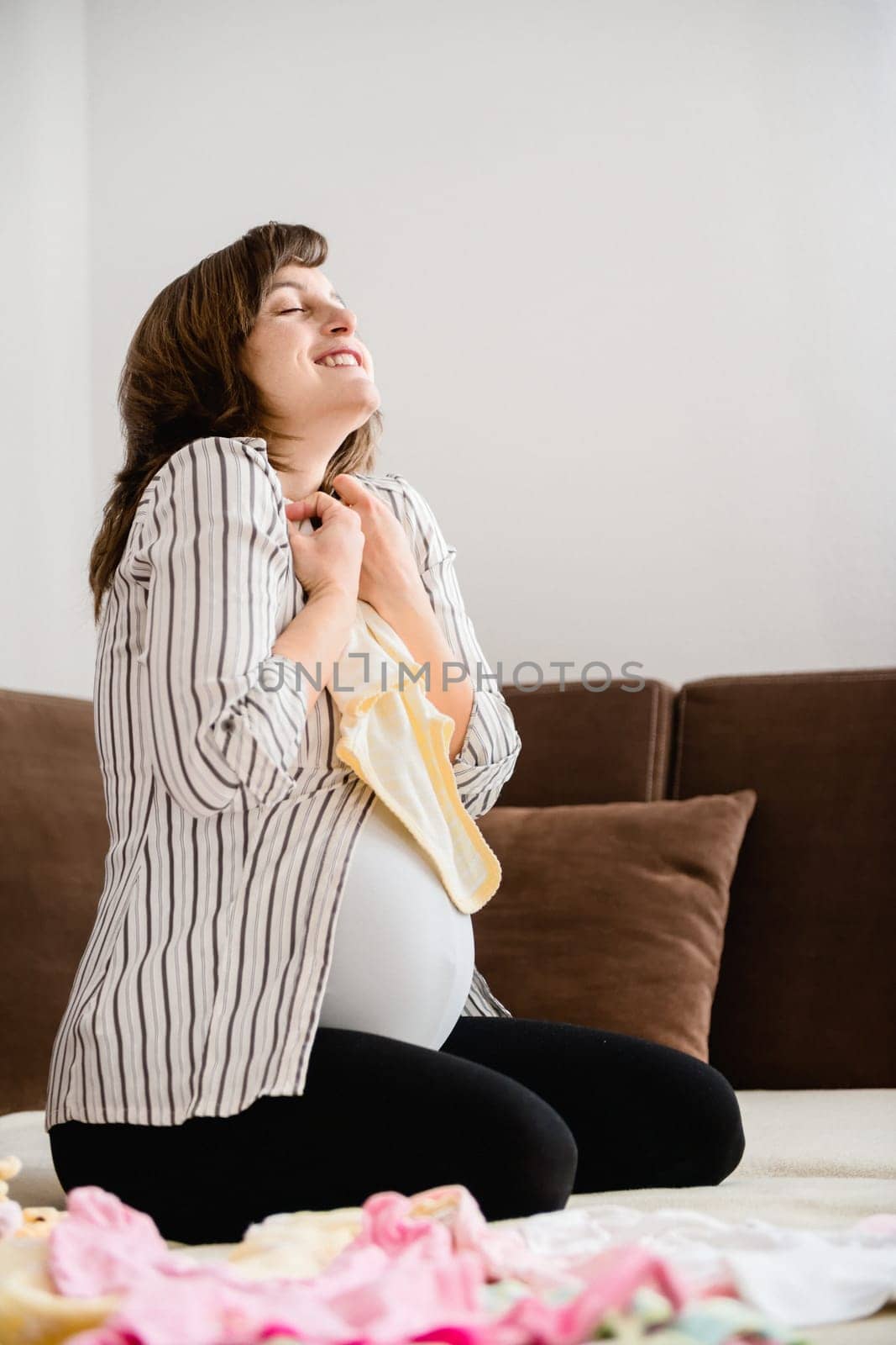 Pregnancy - woman enjoying and preparing baby clothes at home on sofa
