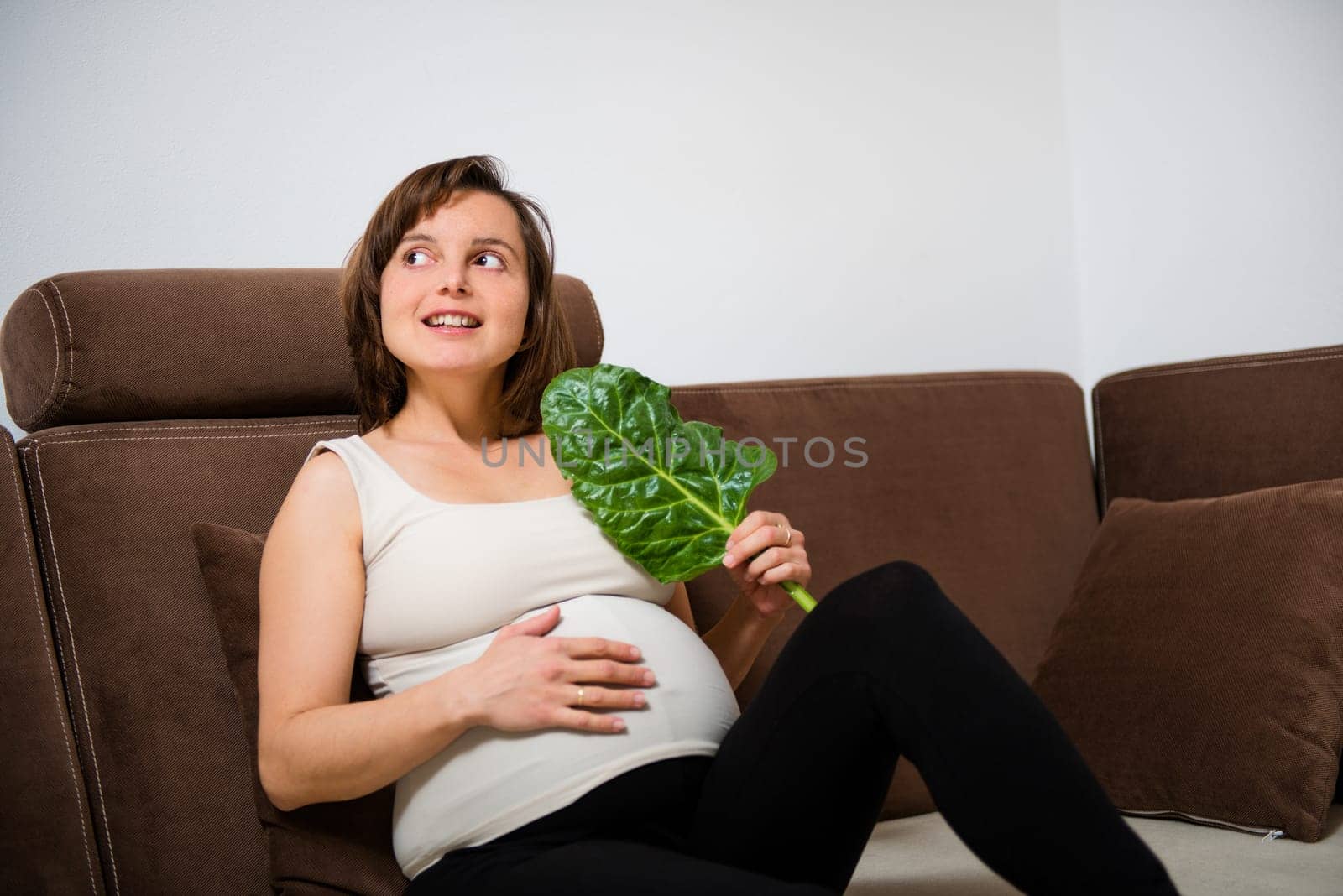 Lifestyle portrait of smiling pregnant woman eating spinach at home