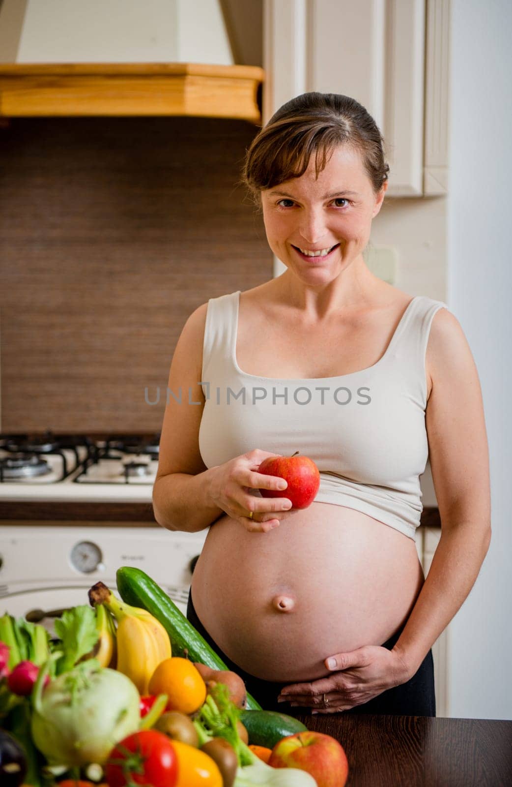 Pregnant woman with abundance of vegetables and fruits holding apple