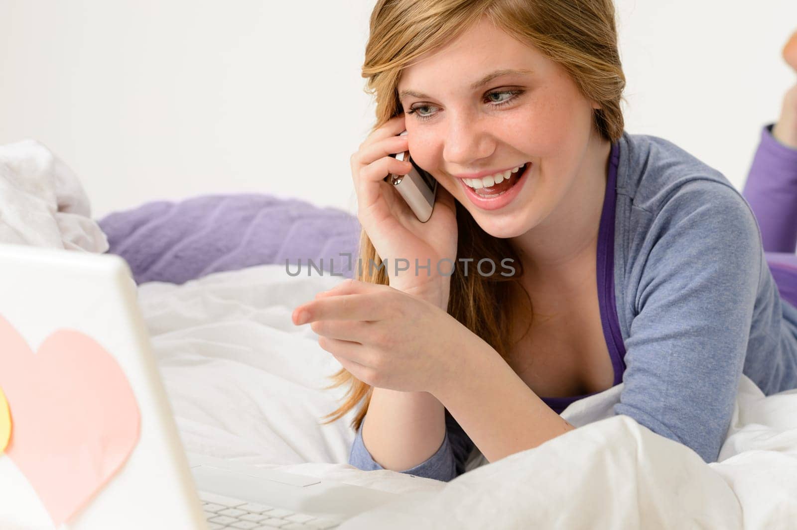 Laughing teenager relaxing by speaking on phone and using laptop